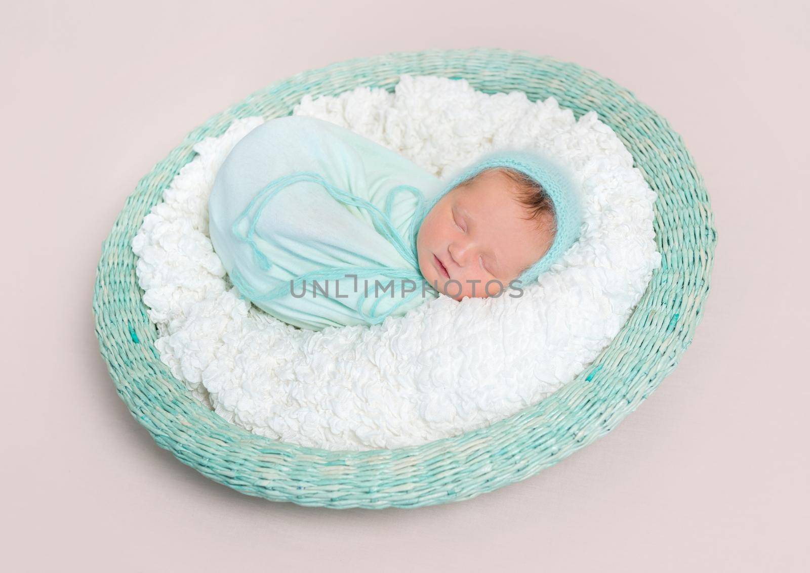 Adorable baby wrapped in blue blanket sleeping on white and blue bedding, in basket, topview