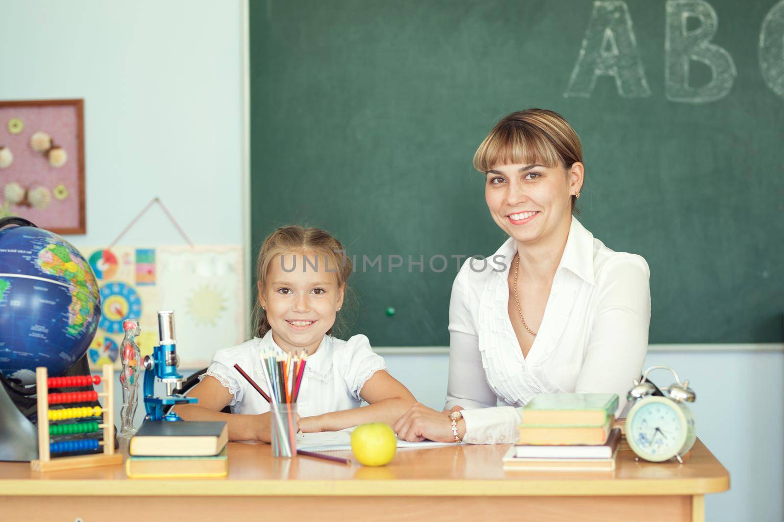 Cute schoolgirl and her teacher in a classroom.