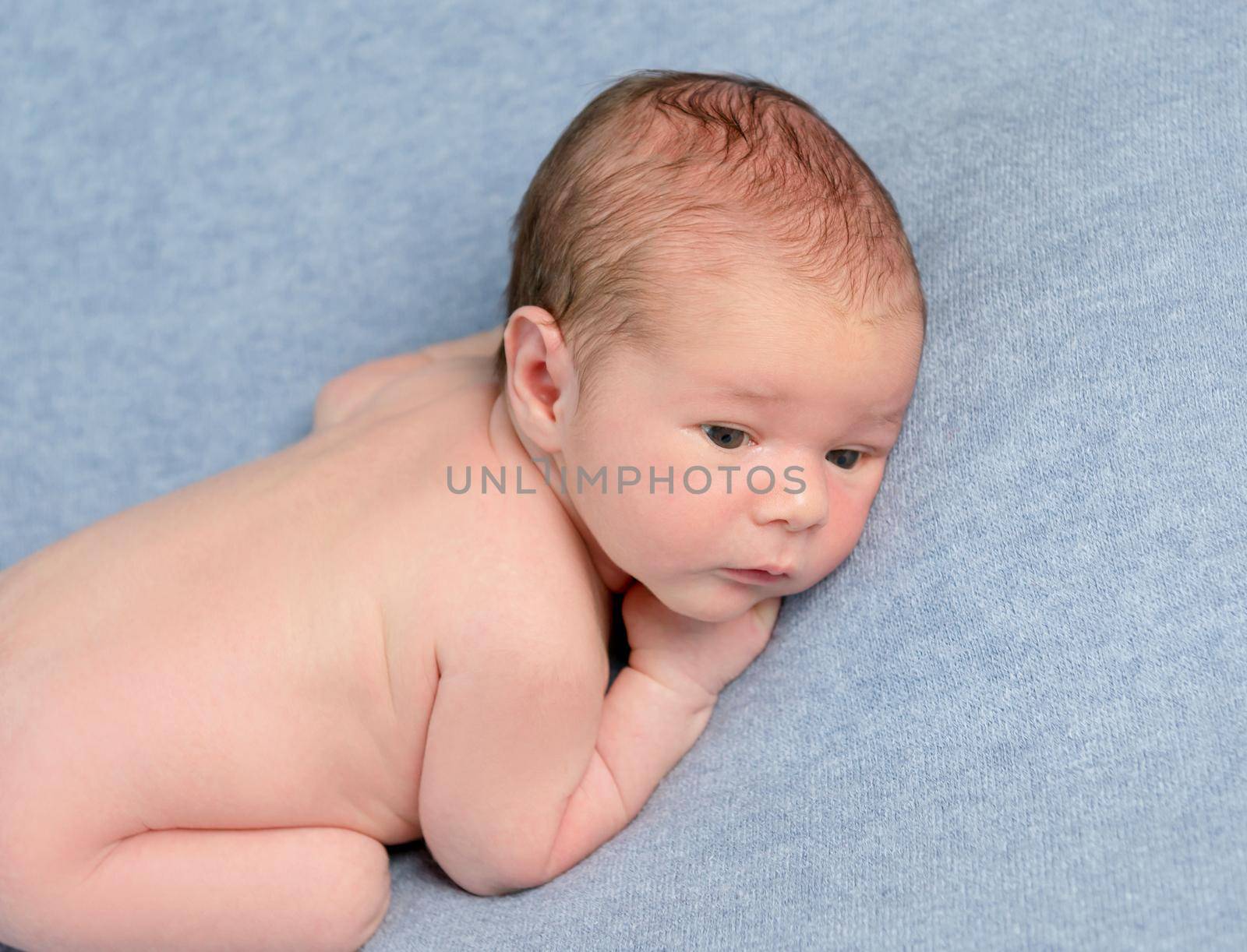 Adorable newborn baby in embryo pose lies on grey blanket.