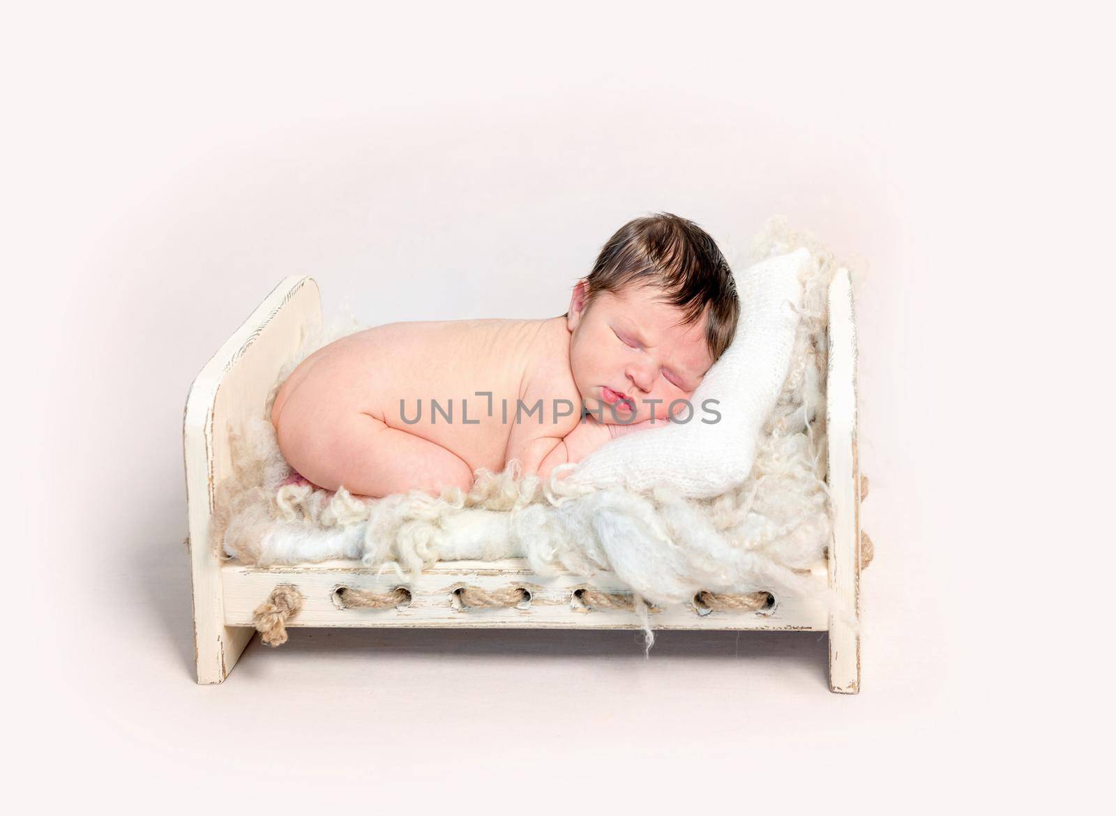 Adorable newborn baby sleeping on his stomach on wooden crib covered with furry rug