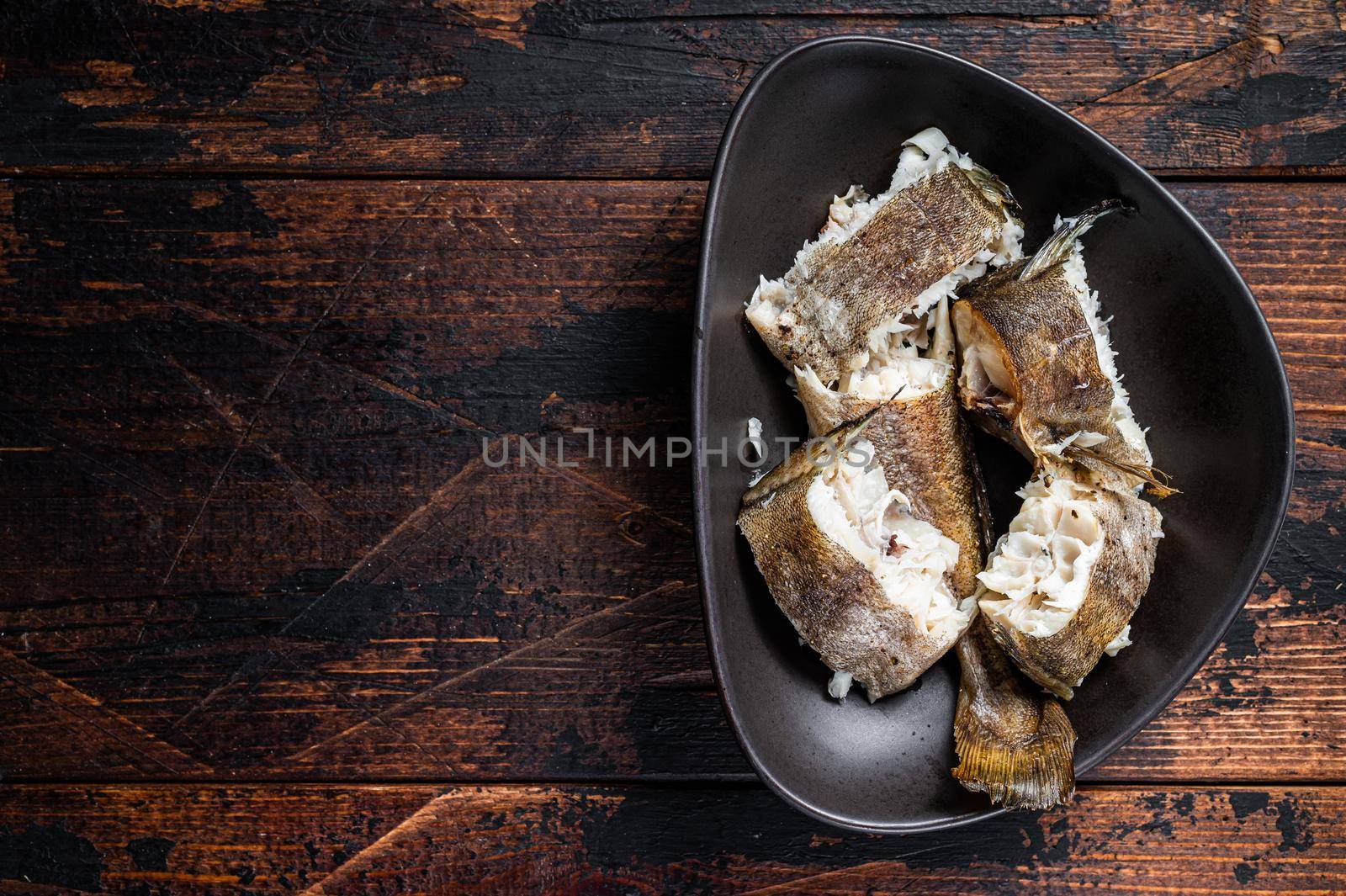 Roasted hake white fish in a plate. Dark wooden background. Top view. Copy space.