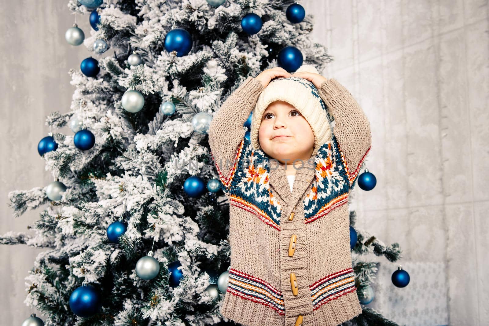 Christmas theme and children. Little Caucasian boy child in a warm hat and sweater posing, eating sweetness, dirty face. Christmas morning. New Year's holidays.