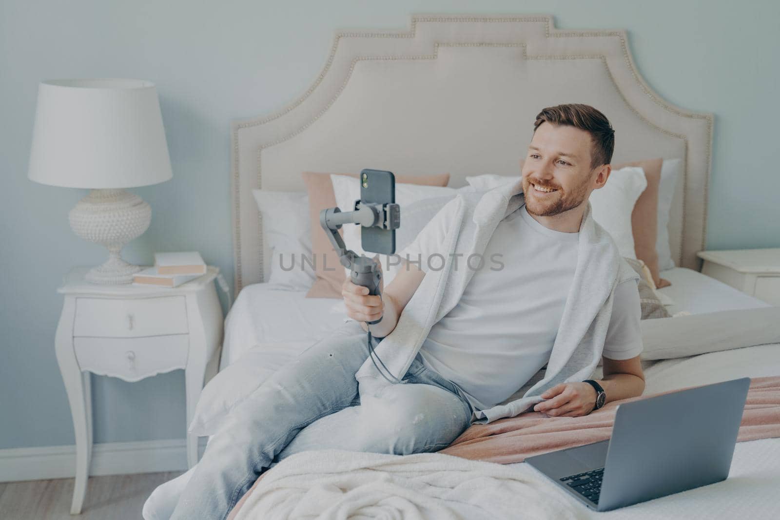 Young man lying on bed while video chatting using phone by vkstock