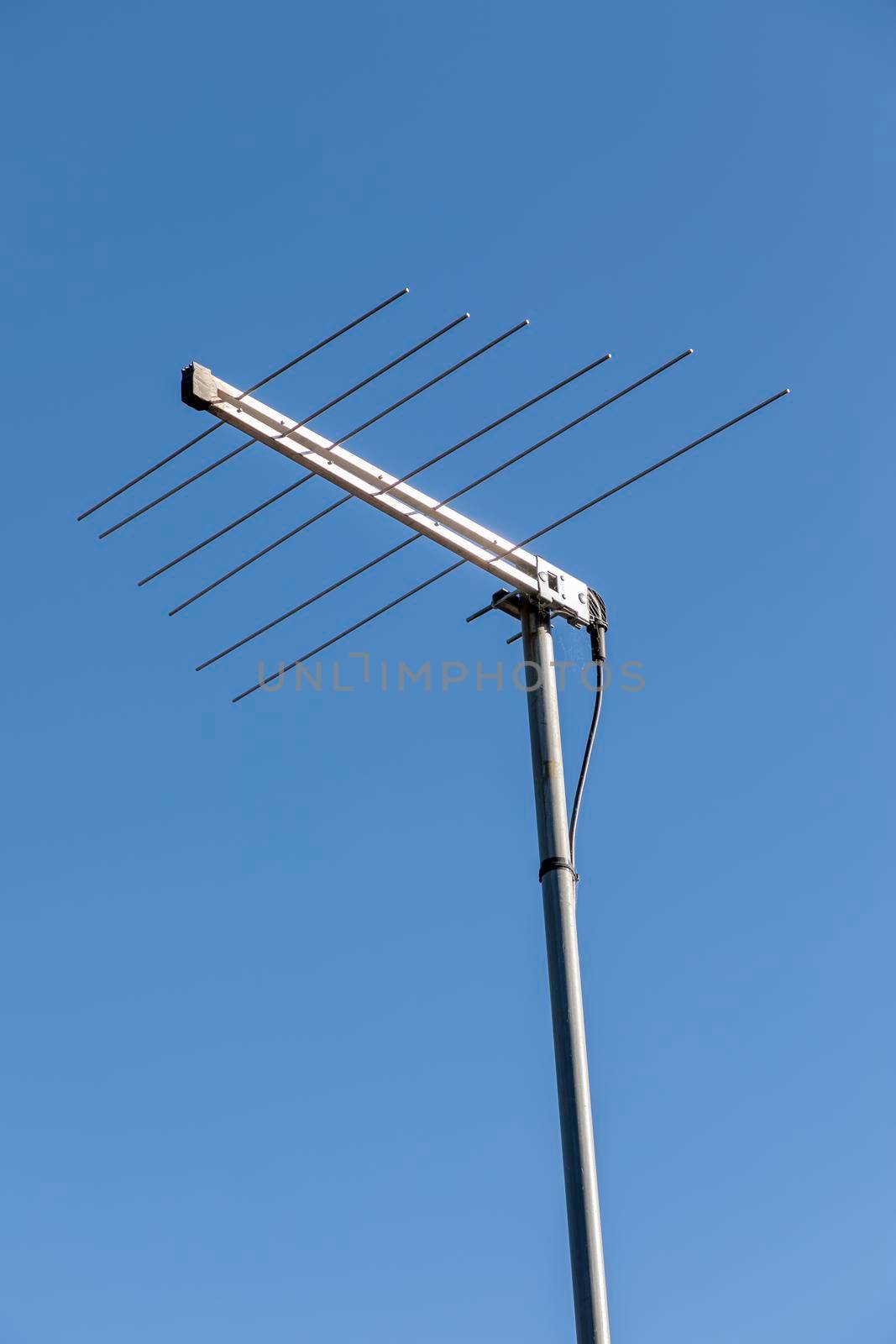 A metal television antenna on a a house roof against a blue sky background