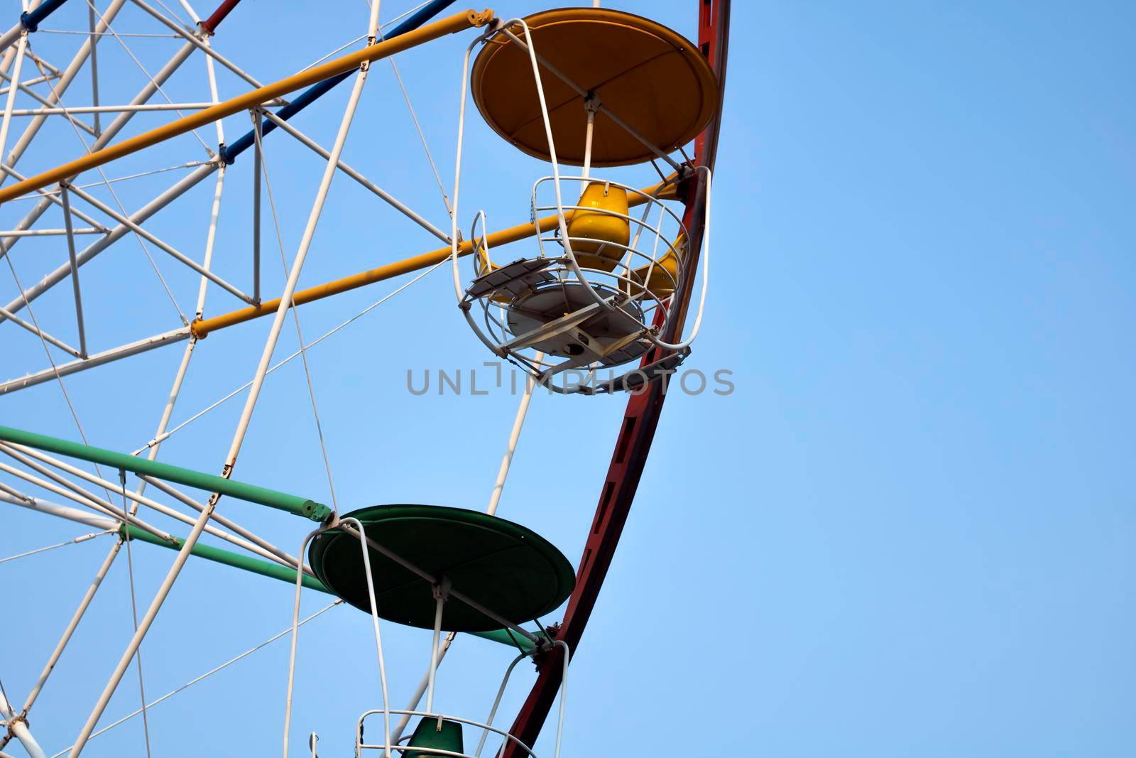 Close-up of a multi-colored Ferris wheel in an amusement park against a background of blue sky