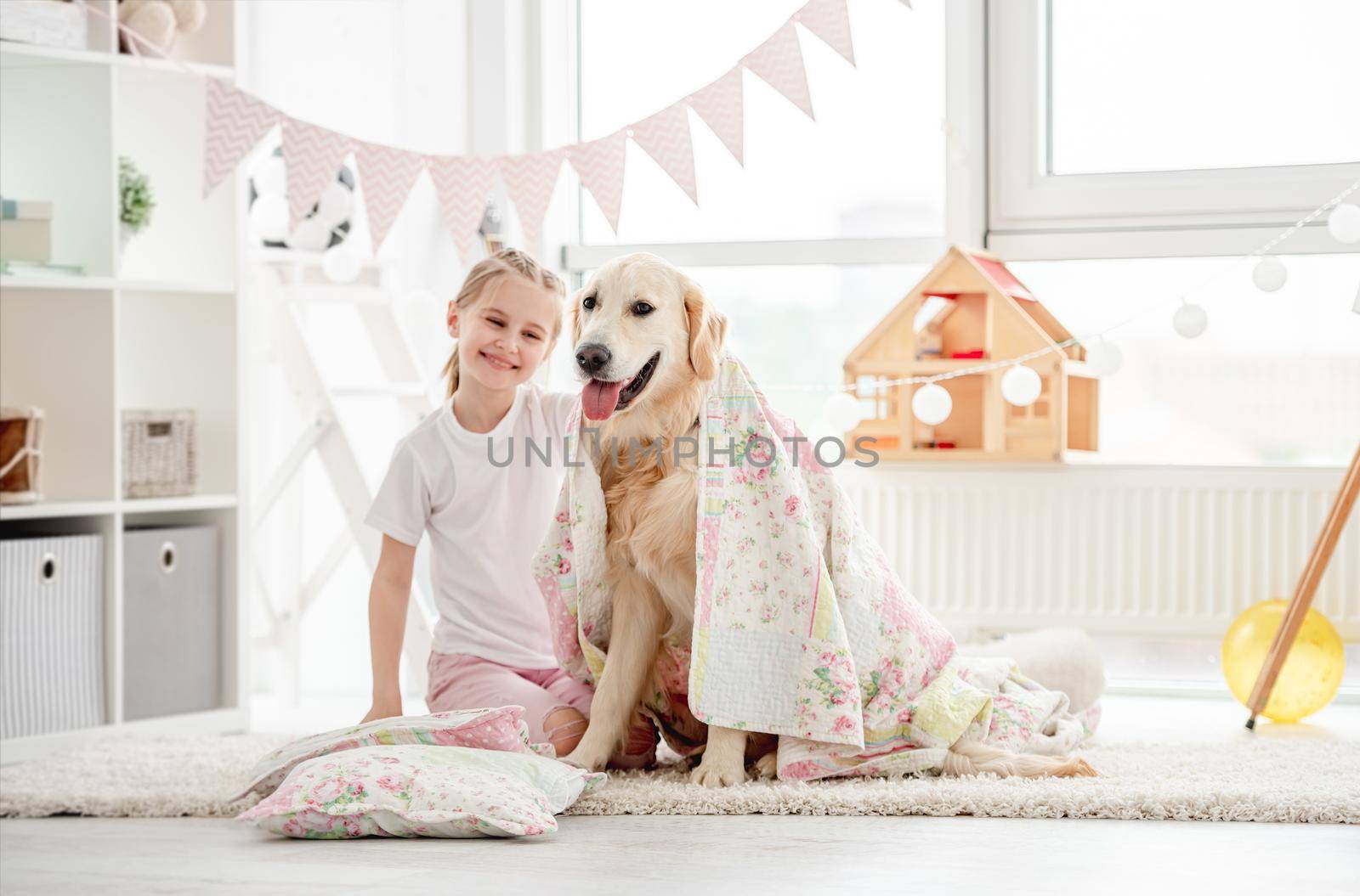 Smiling little girl having fun with cute dog and bedding in kids room