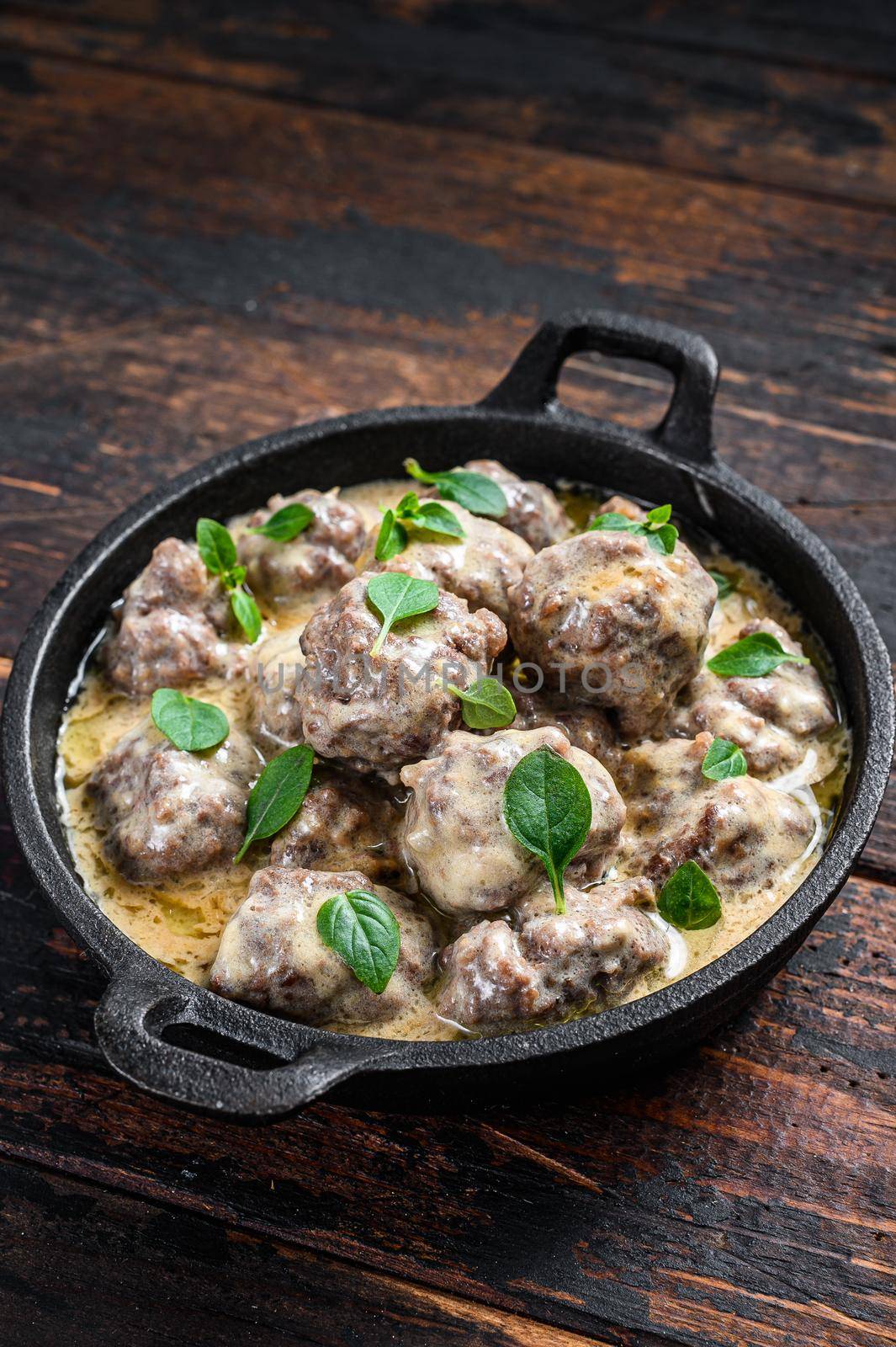 Beef meatballs in cream sauce in a frying pan. Dark wooden background. Top view.