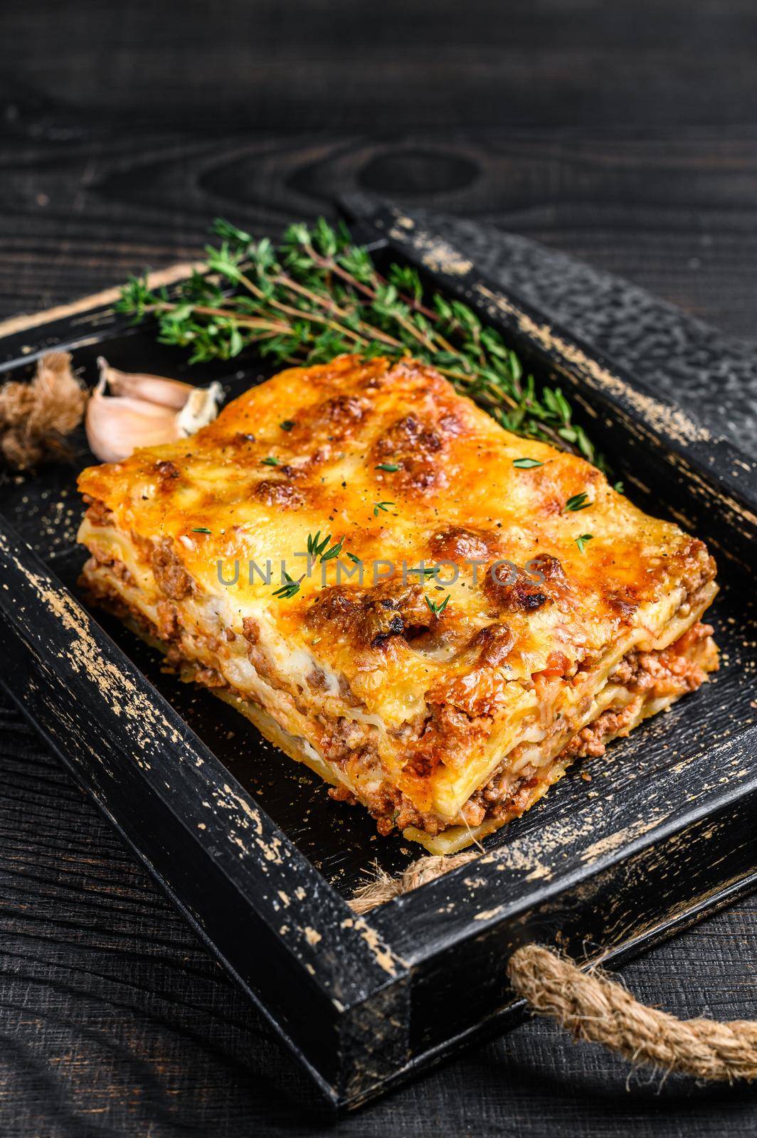 Portion of Lasagna with mince beef meat and tomato bolognese sauce in a wooden tray. Black wooden background. Top view.