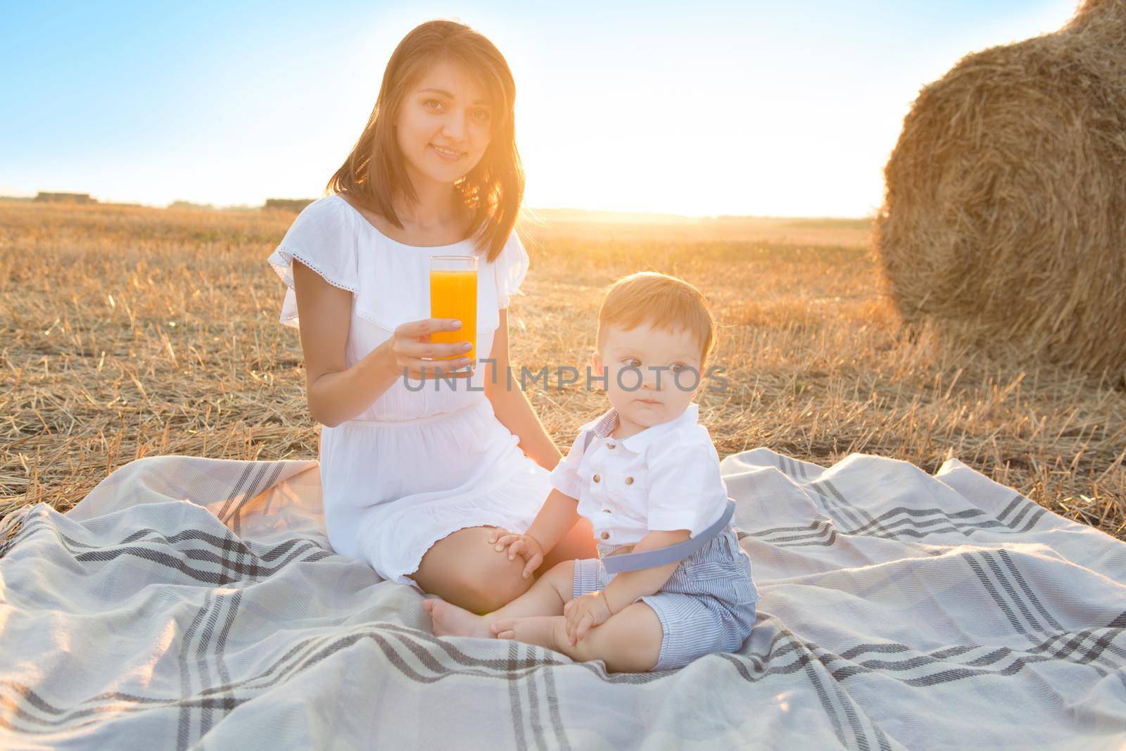 Mother and her son on holiday at a picnic. Mom is drinking orange juice. Happy family relaxing in nature. Healthy eating.