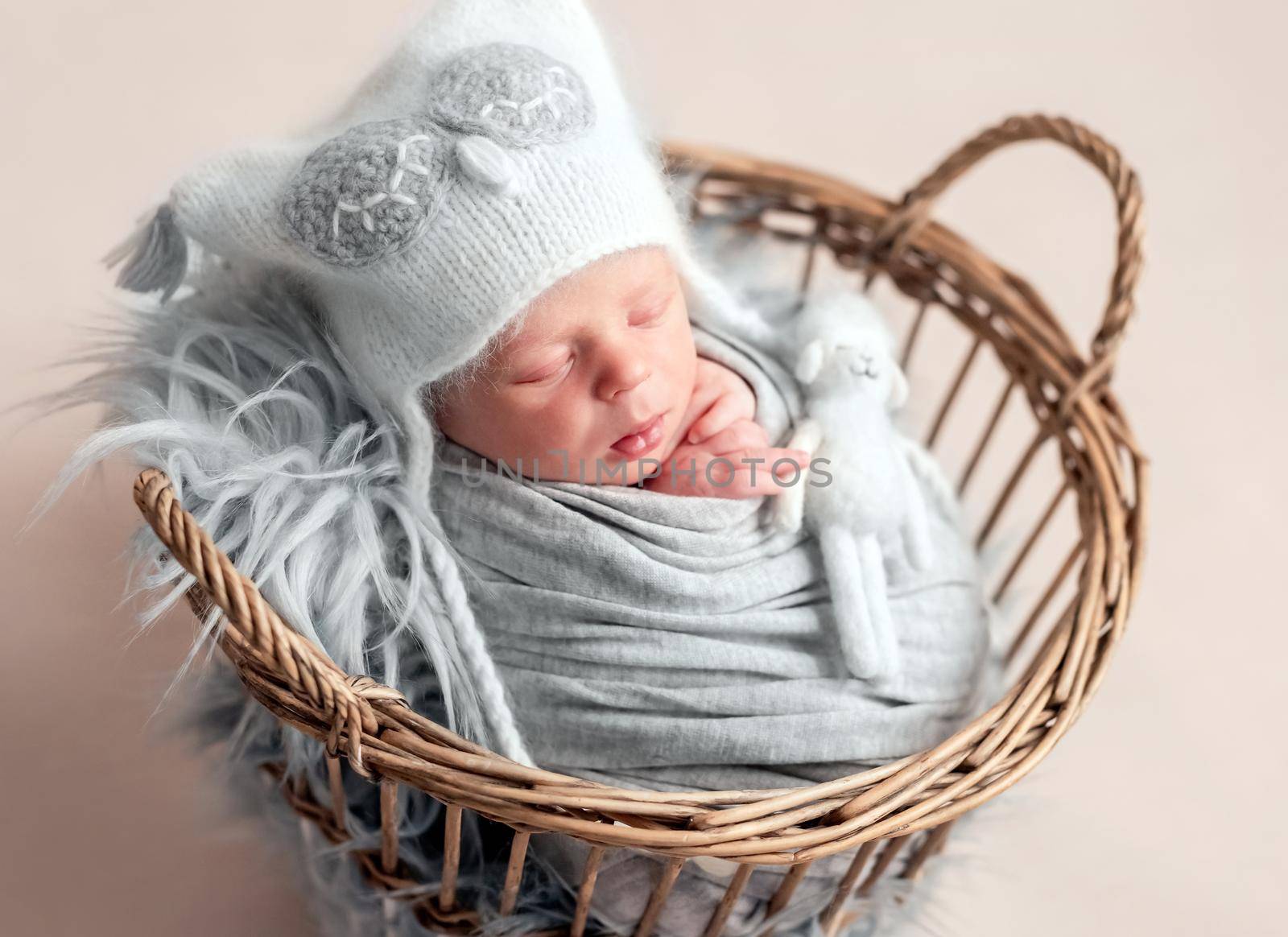 Top view of baby in white knitted hat sleeping in basket covered in blanket