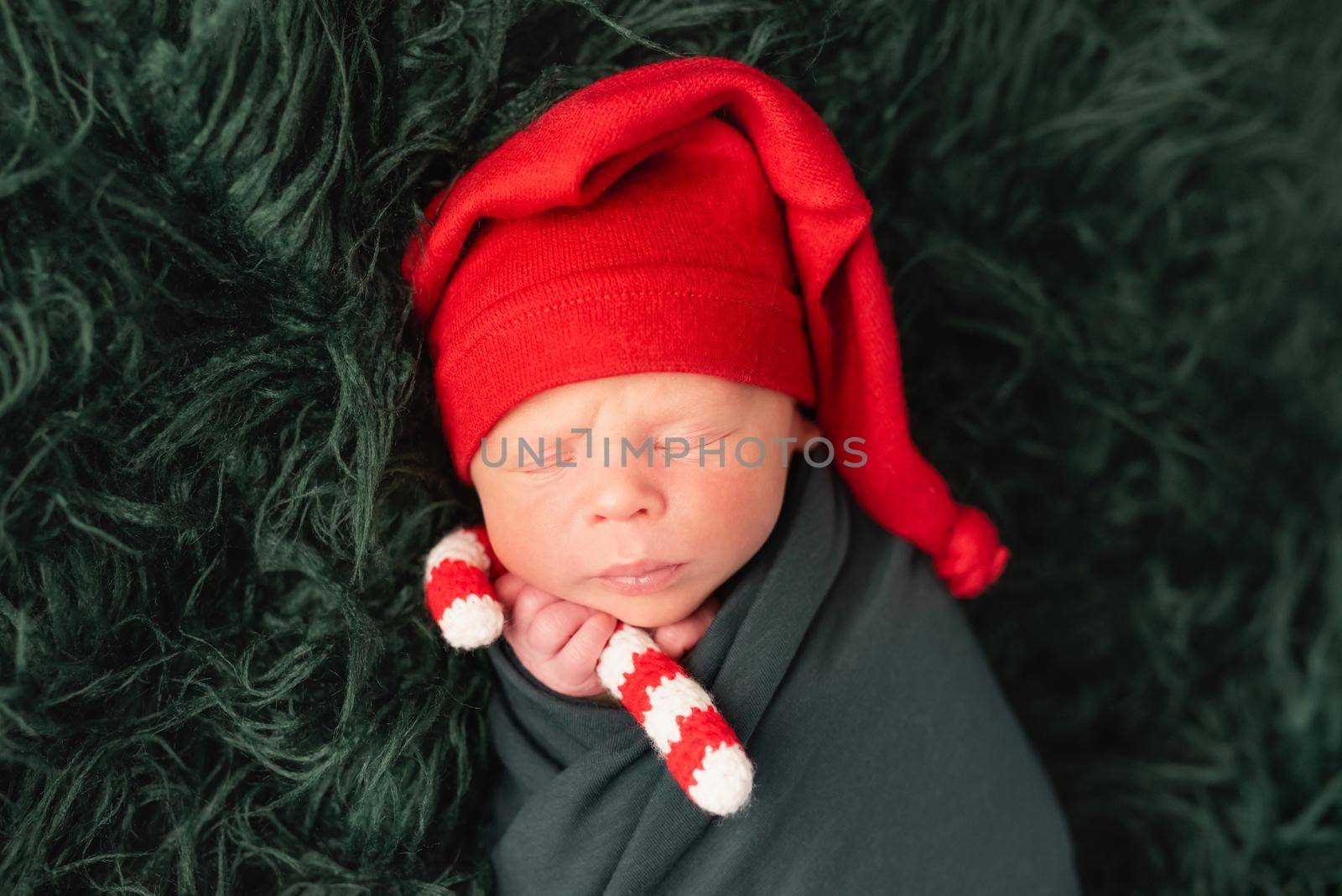 Cute baby in red santa hat sleeping with knitted candy stick