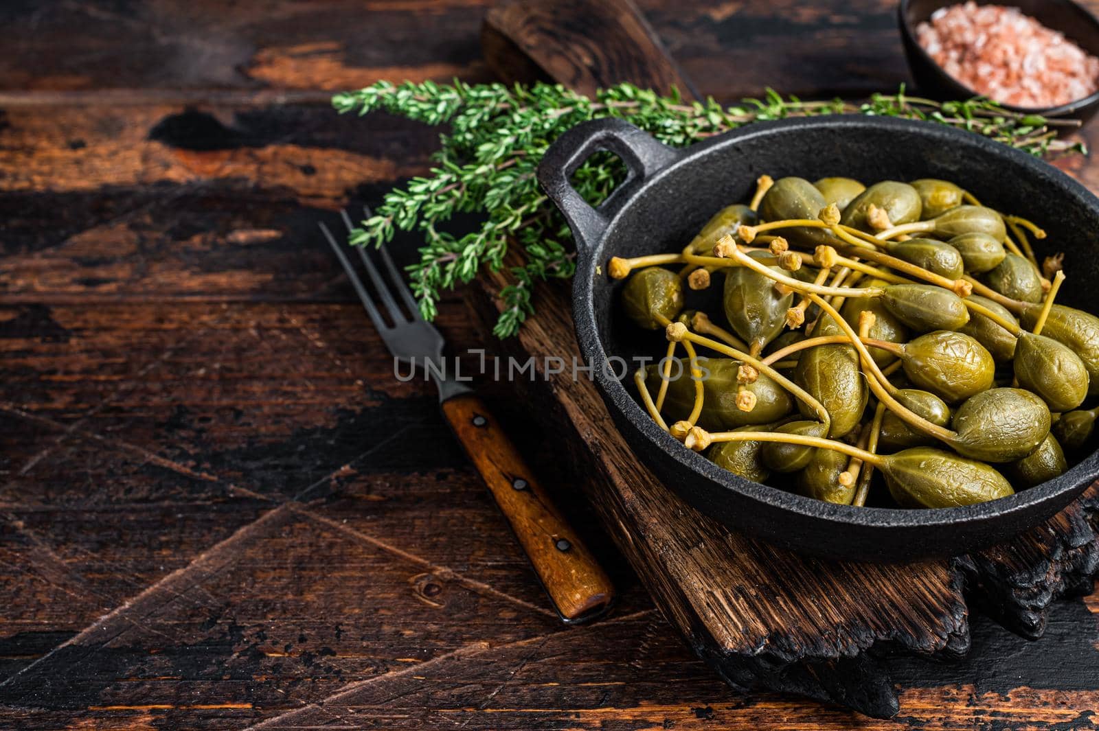 Marinated canned capers in a pan. Dark wooden background. Top view. Copy space.