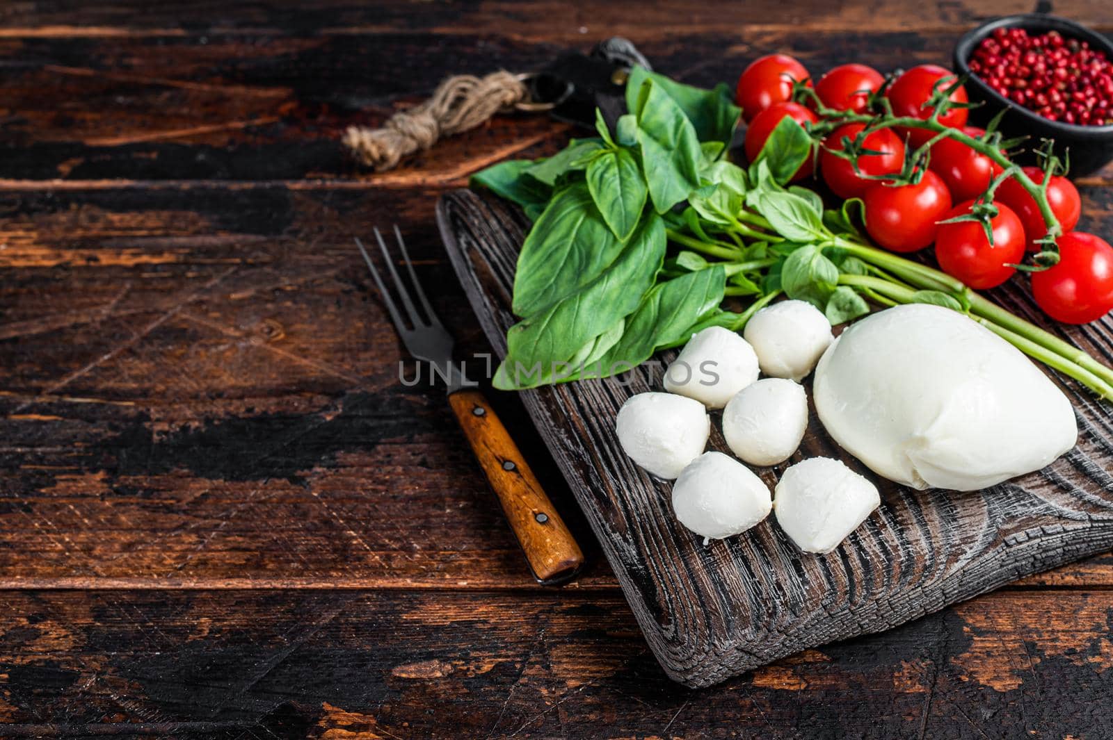 Mozzarella cheese, basil and tomato cherry on wooden board, Ingredients for Caprese salad. Dark wooden background. Top view. Copy space.