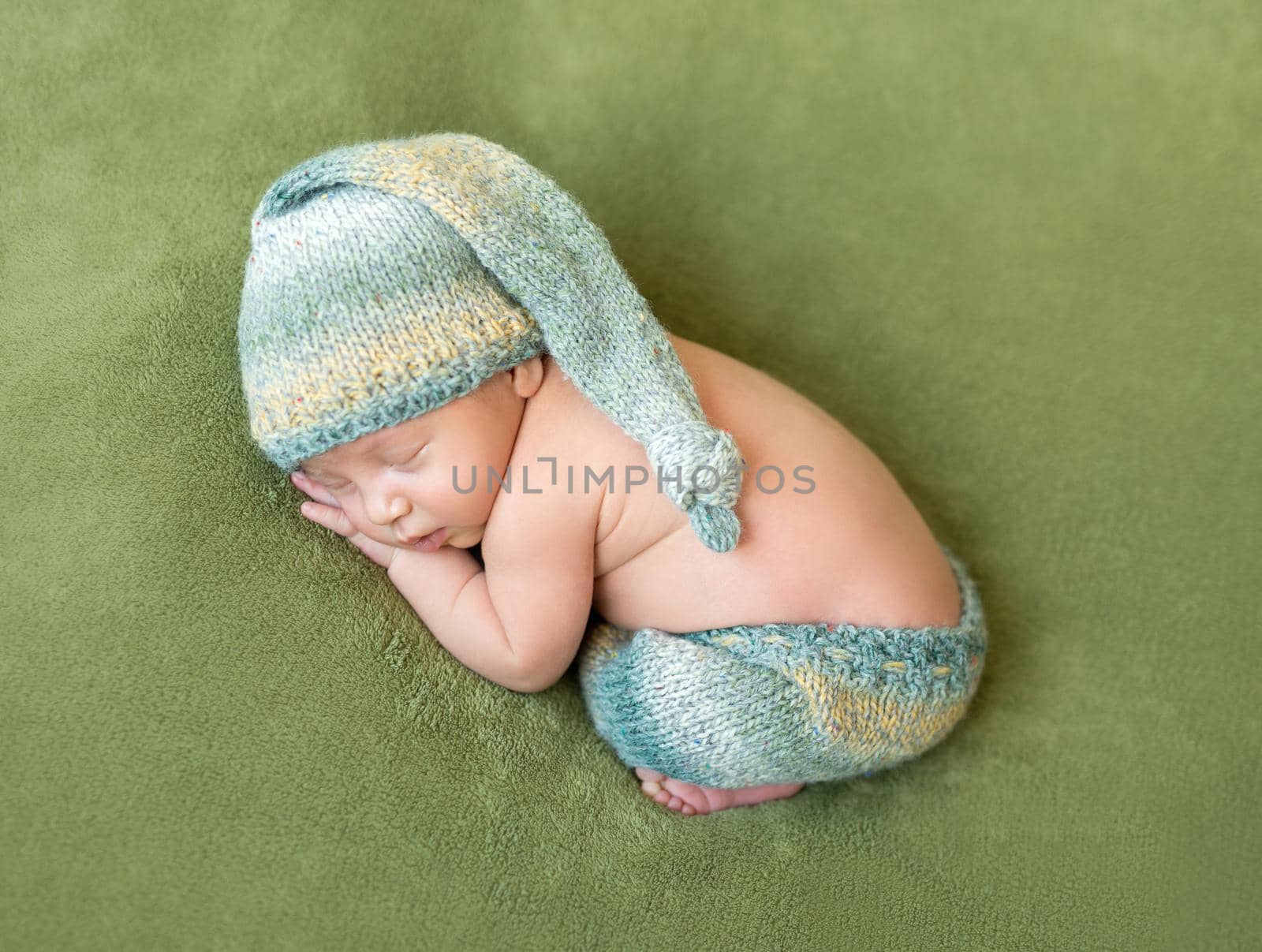 lovely newborn baby in knitted hat and panties sleeps curled up, top view