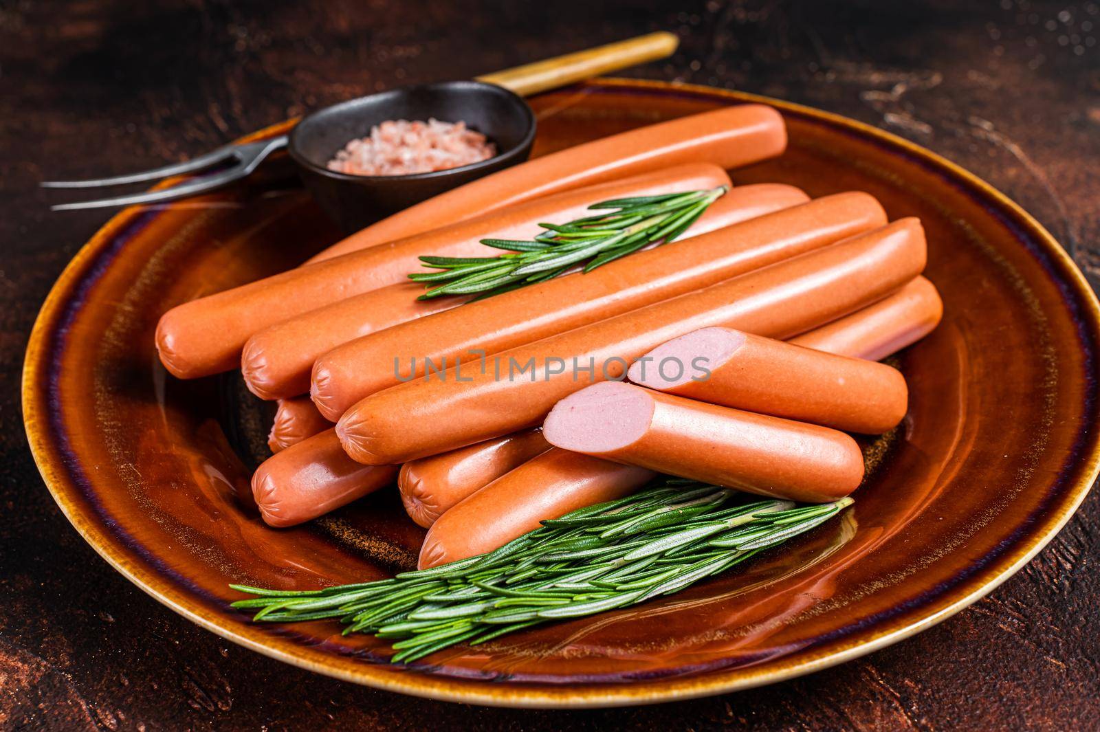 Frankfurter raw sausages in a rustic plate with herbs. Dark background. Top view by Composter