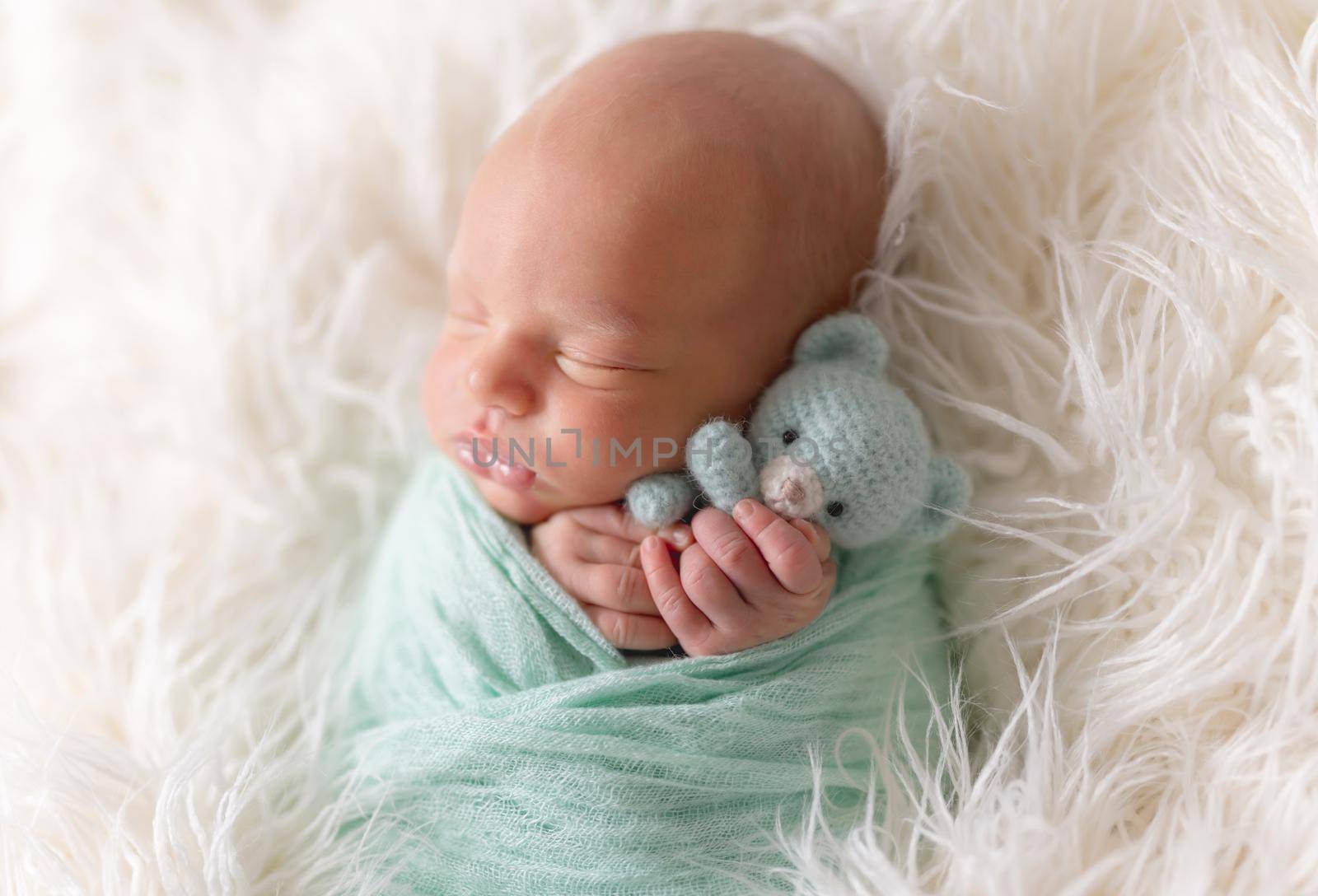 Newborn boy lying wrapped in a blanket with favorite knitted blue teddy bear