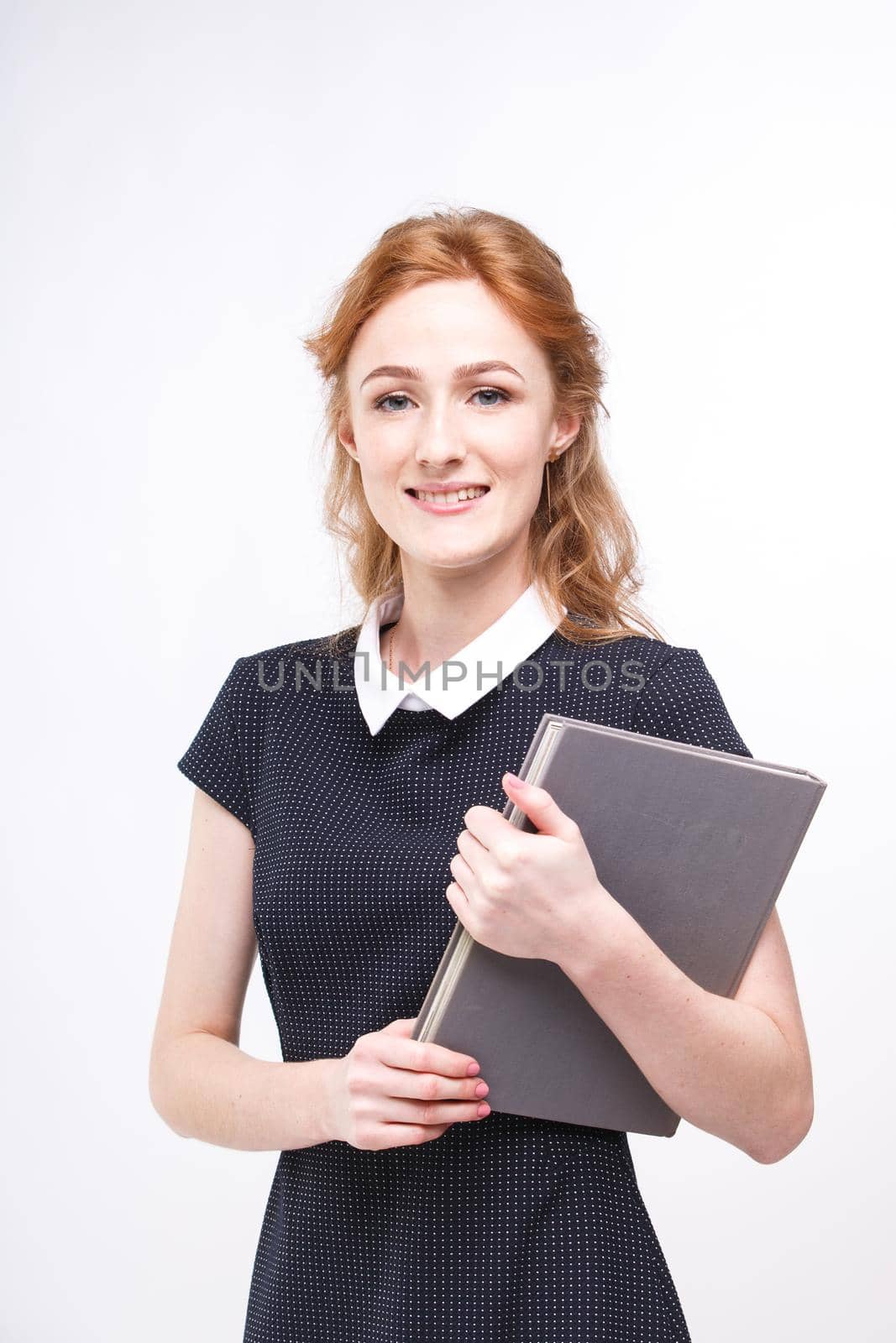 Beautiful girl with red hair and gray book in hands dressed in black dress on white isolated background by Tomashevska