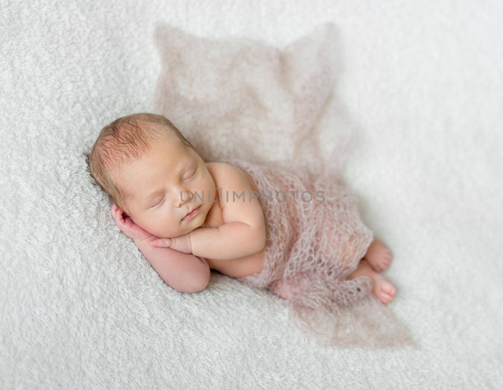 lovely smiling sleeping baby covered with light knitted shawl on white blanket