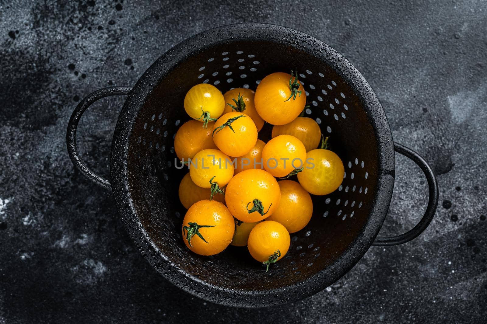 Yellow cherry tomato in a colander. Black background. Top view.