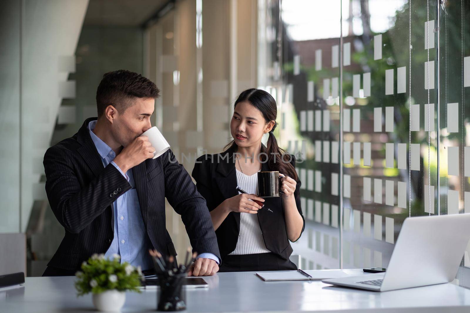 Friendly male leader laughing at group business meeting, happy young businesswoman enjoying fun conversation with partner, smiling business coach executive talking to colleague.