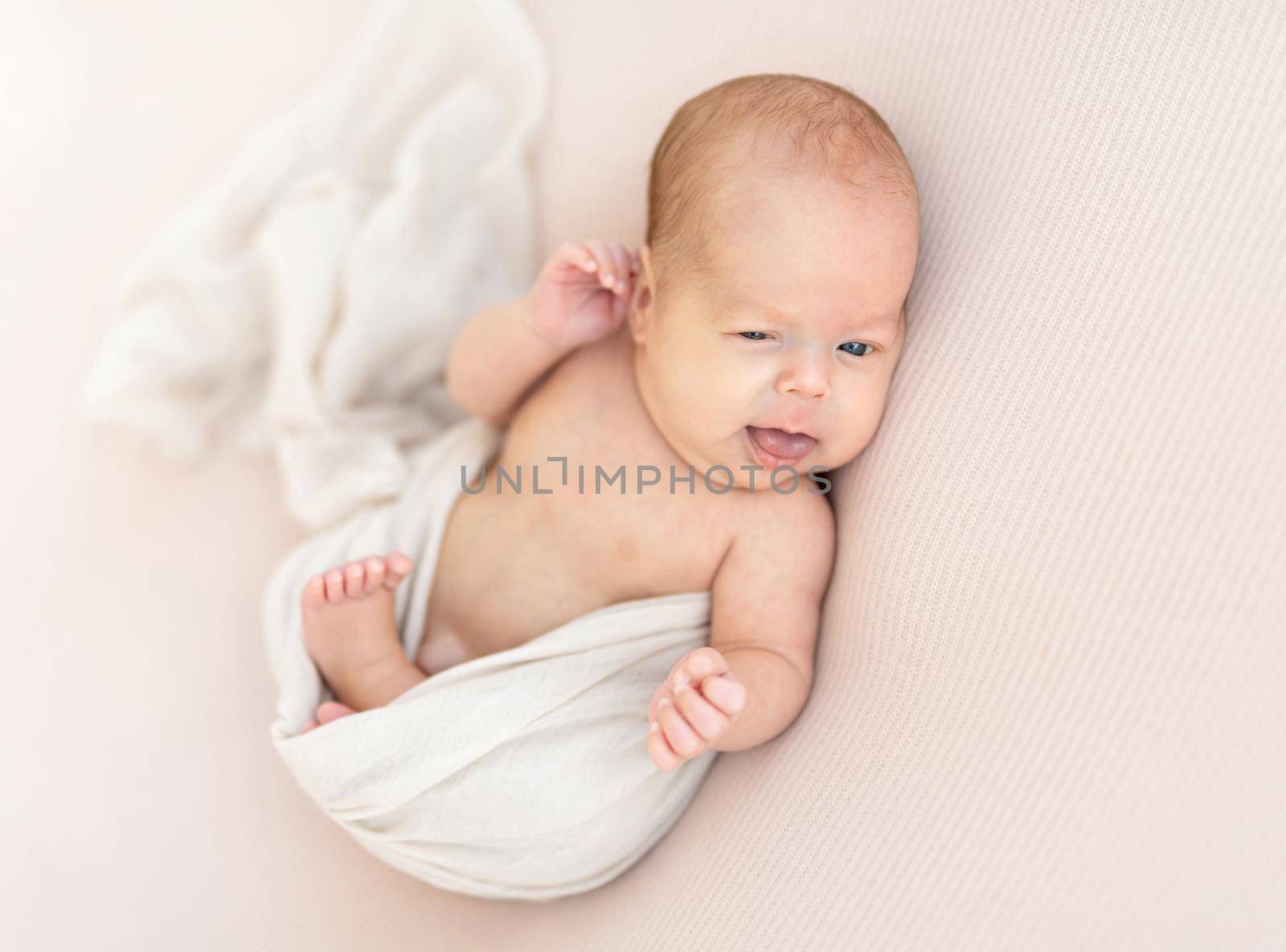 Cute awake newborn touching his ear with hand