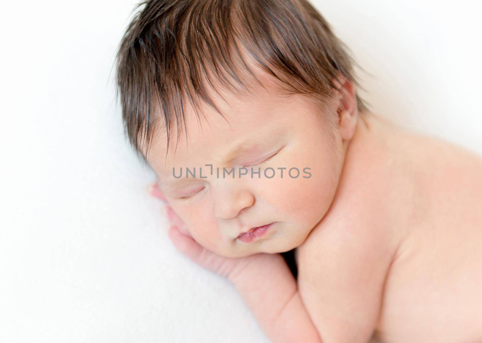 Portrait of sweet newborn baby sleeping with hand under the head on white blanket