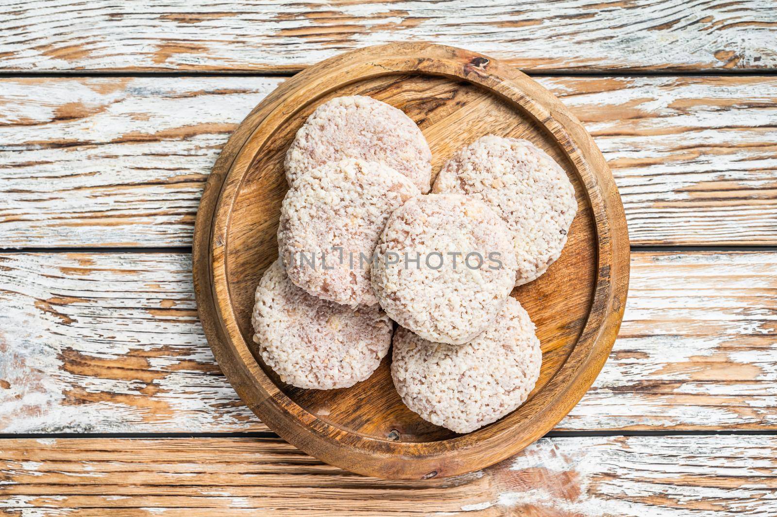 Raw chicken patty cutlet with breadcrumbs. White wooden background. Top view.