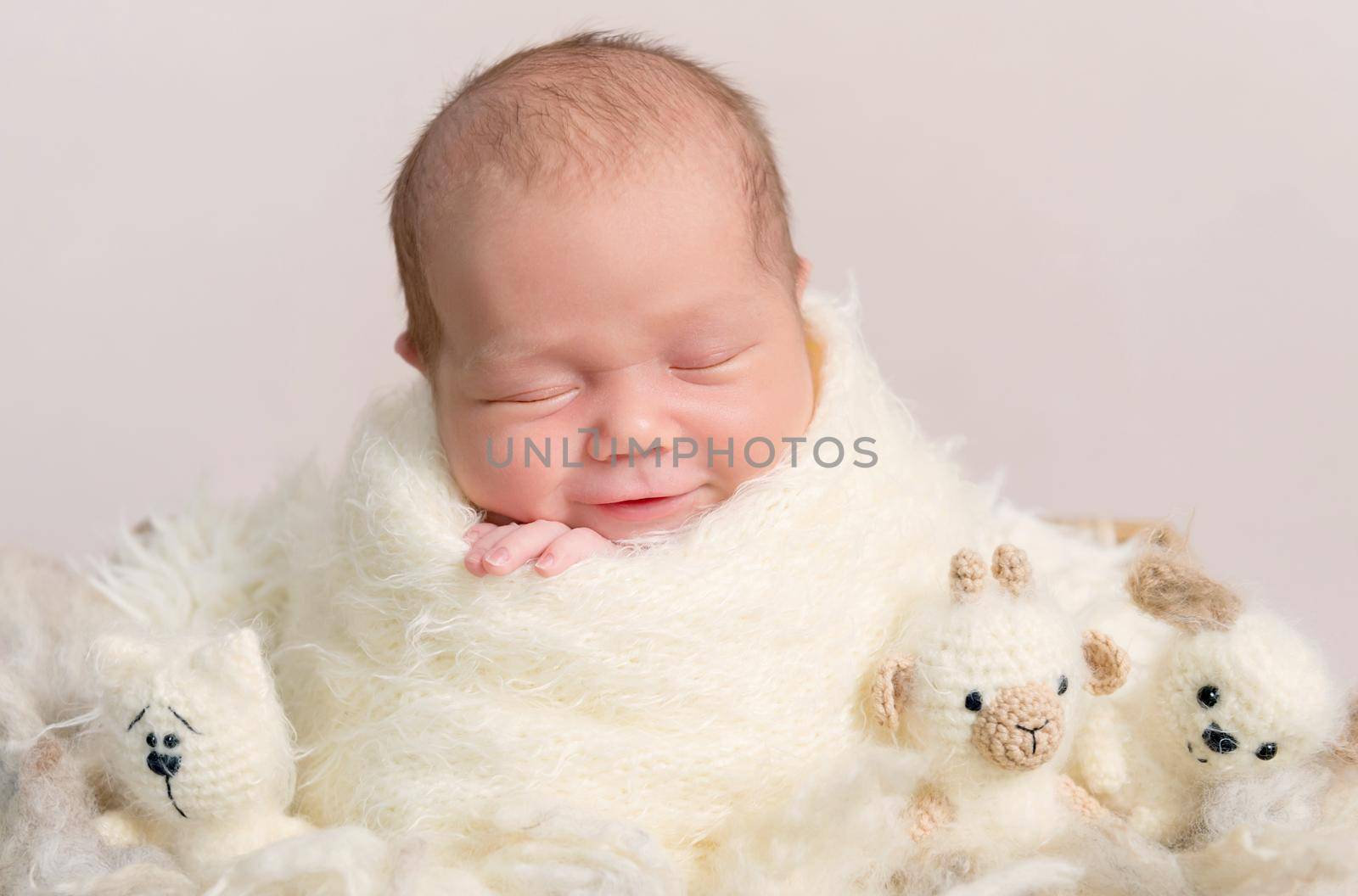 Portrait of smiling gorgeous baby asleep in soft beige wrap with plush toys around