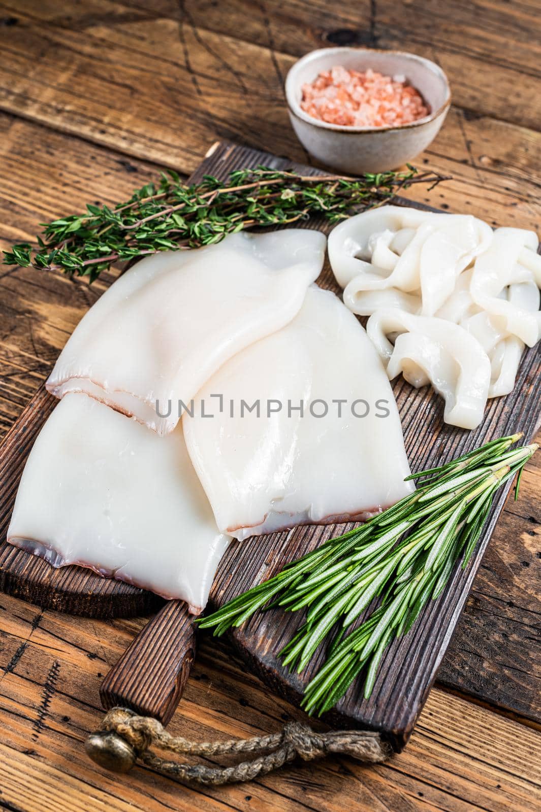 Sliced rings Raw Calamari or Squid on a wooden board with rosemary. wooden background. Top view.