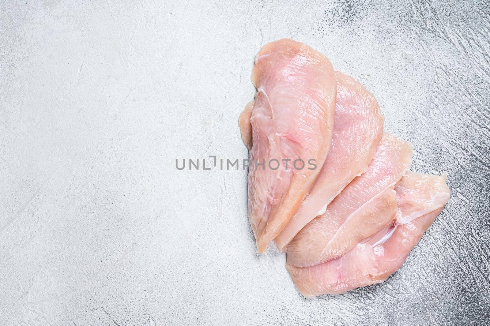 Raw sliced chicken breast fillet steaks. White background. Top view. Copy space by Composter