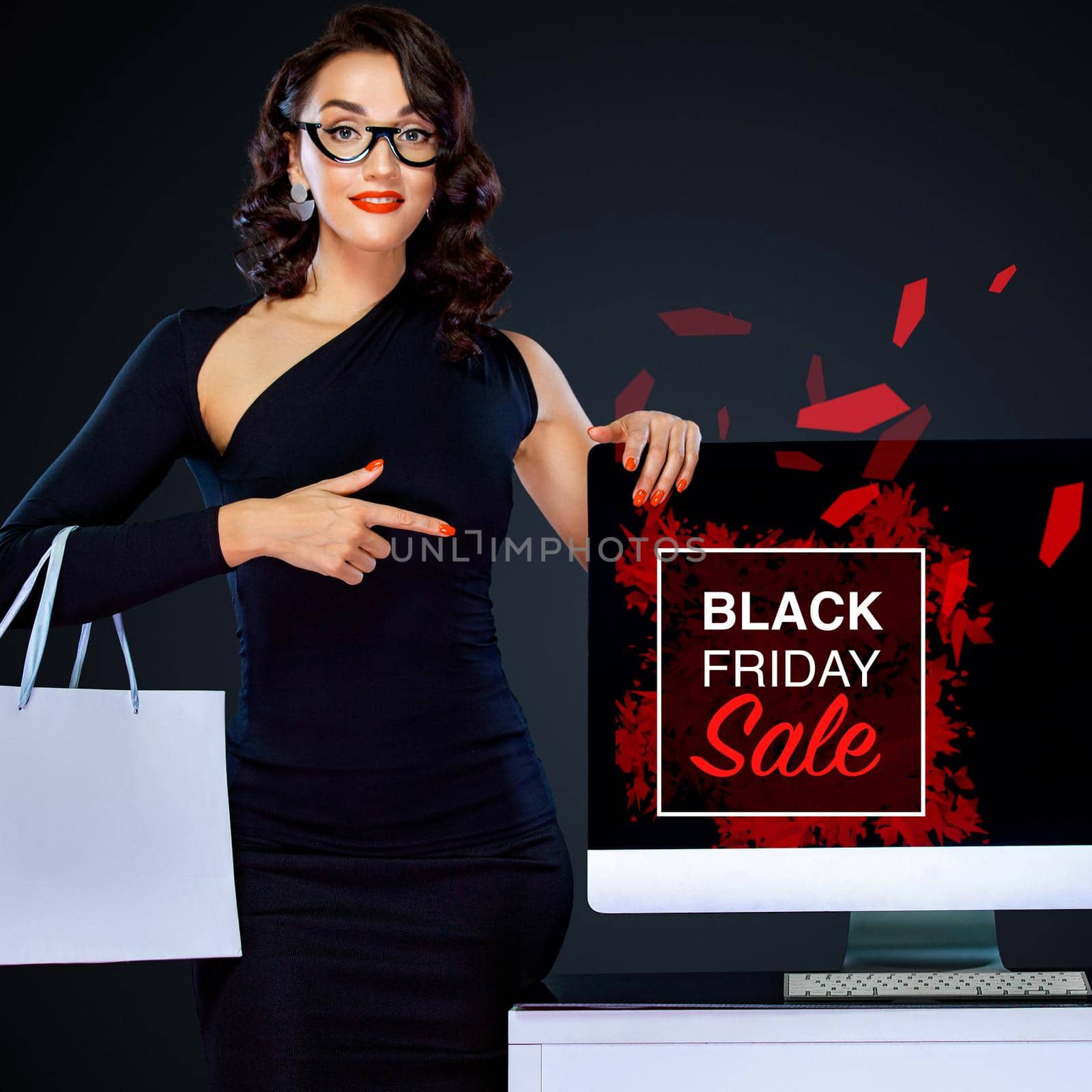 Black friday and Cyber Monday sale concept for shop. Shopping woman holding white bag and pointing on computer isolated on dark background by MikeOrlov