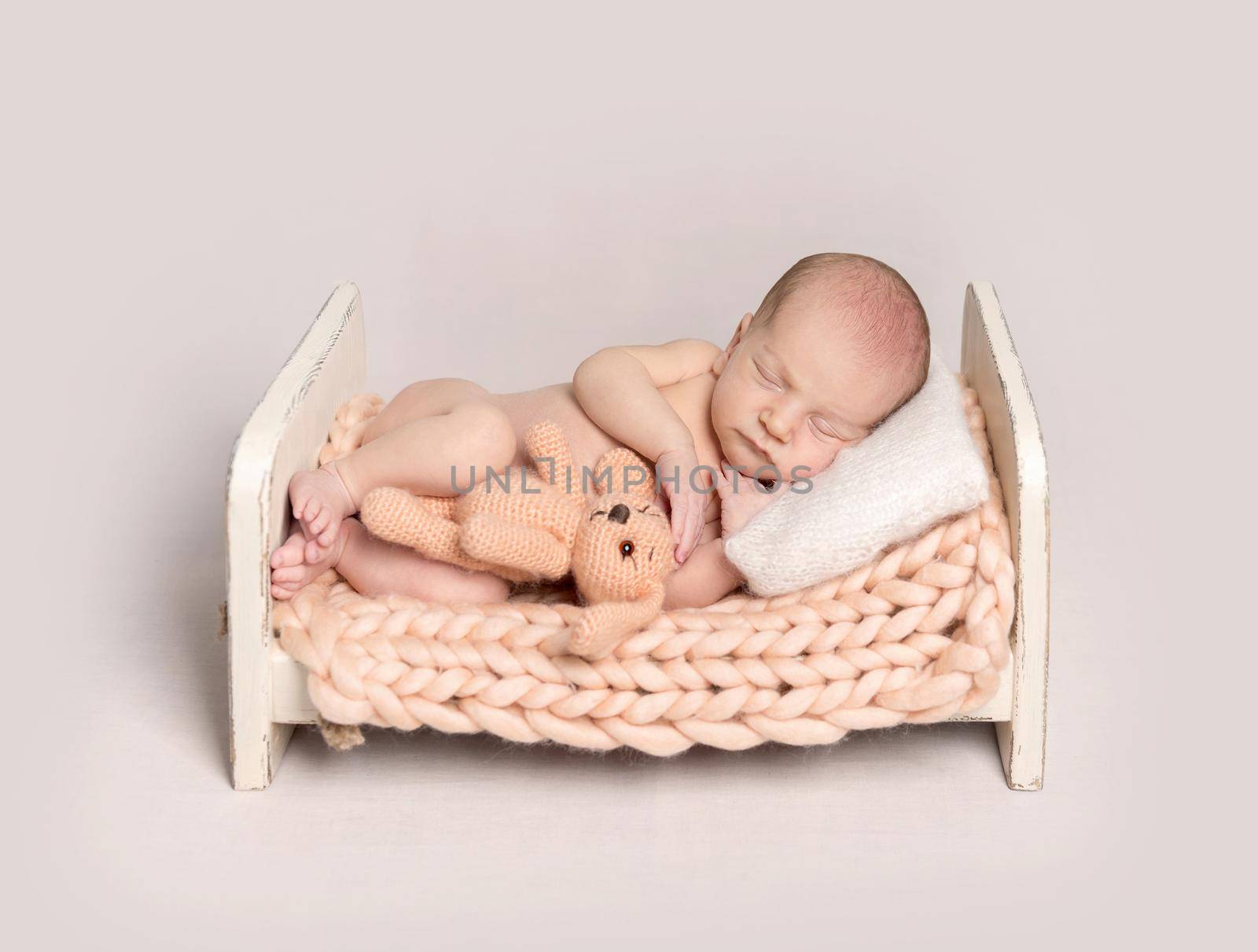 Newborn baby fall asleep on a small bed covered with knitted rug and holds puppy toy