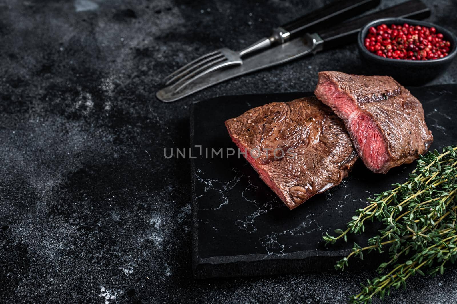 Grilled Top Blade or flat iron roast beef meat steaks on marble board. Black background. Top View. Copy space by Composter