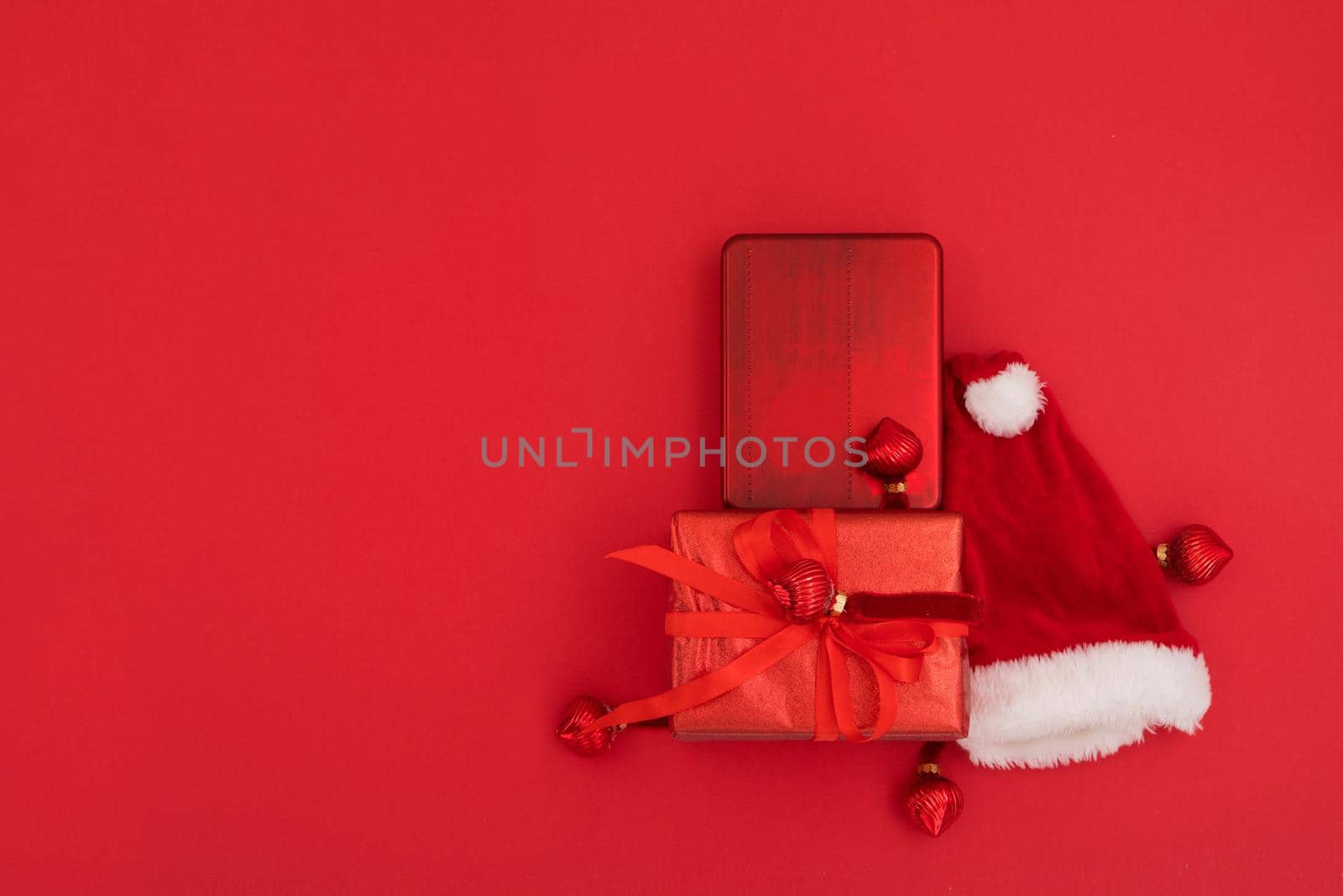 Top view of composition of traditional Santa hat placed near wrapped gifts on Christmas day against red background