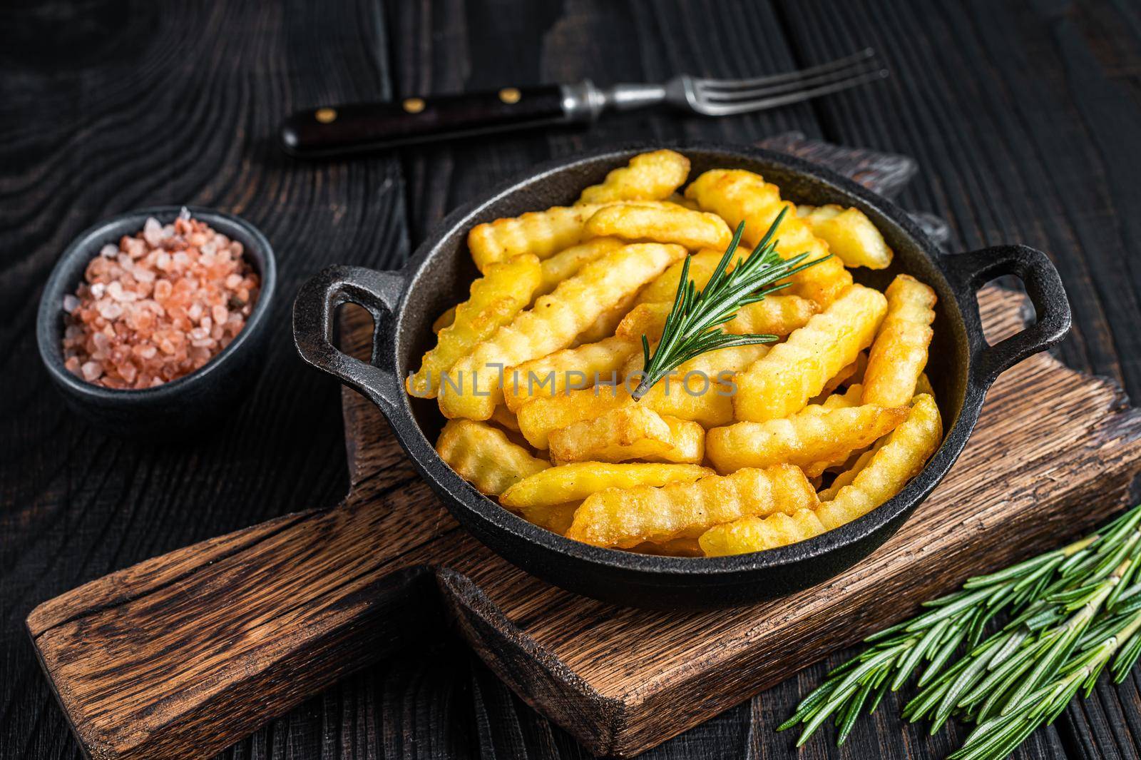 Fried Crinkle French fries potatoes in a pan. Black Wooden background. Top view by Composter