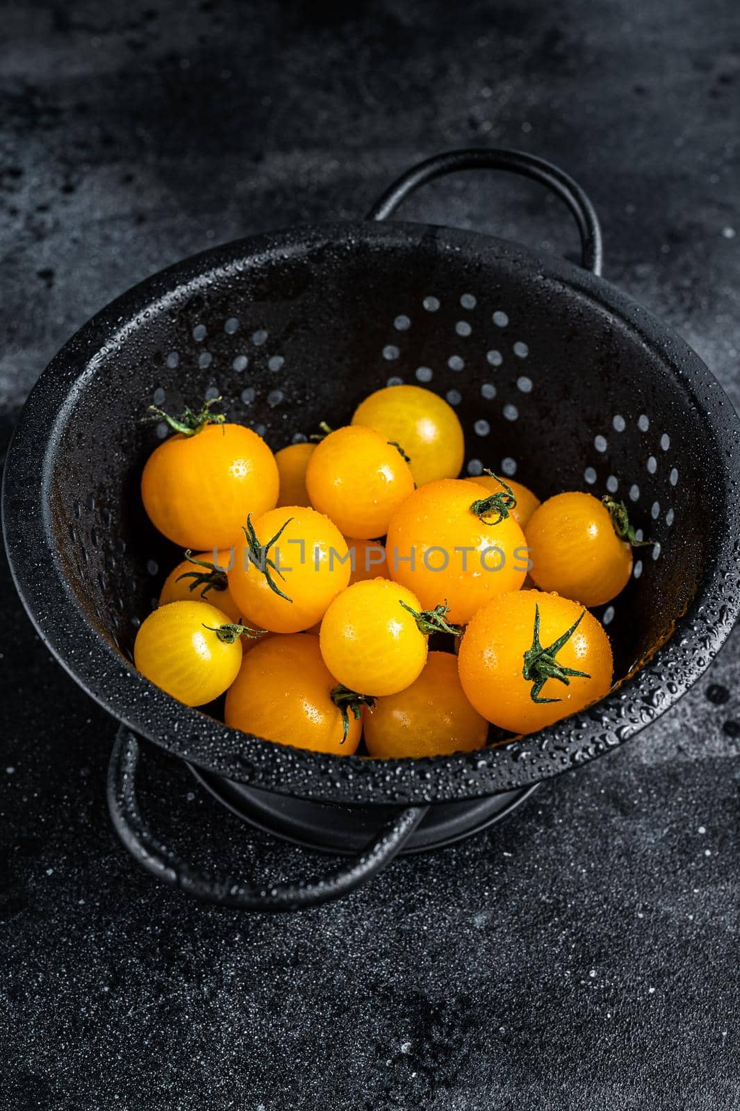 Yellow cherry tomato in a colander. Black background. Top view by Composter