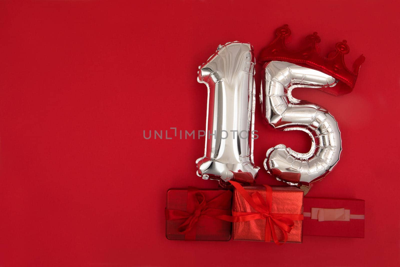 Foil silver air balloons showing number 15 fifteen placed on red background with wrapped presents for concept of birthday anniversary