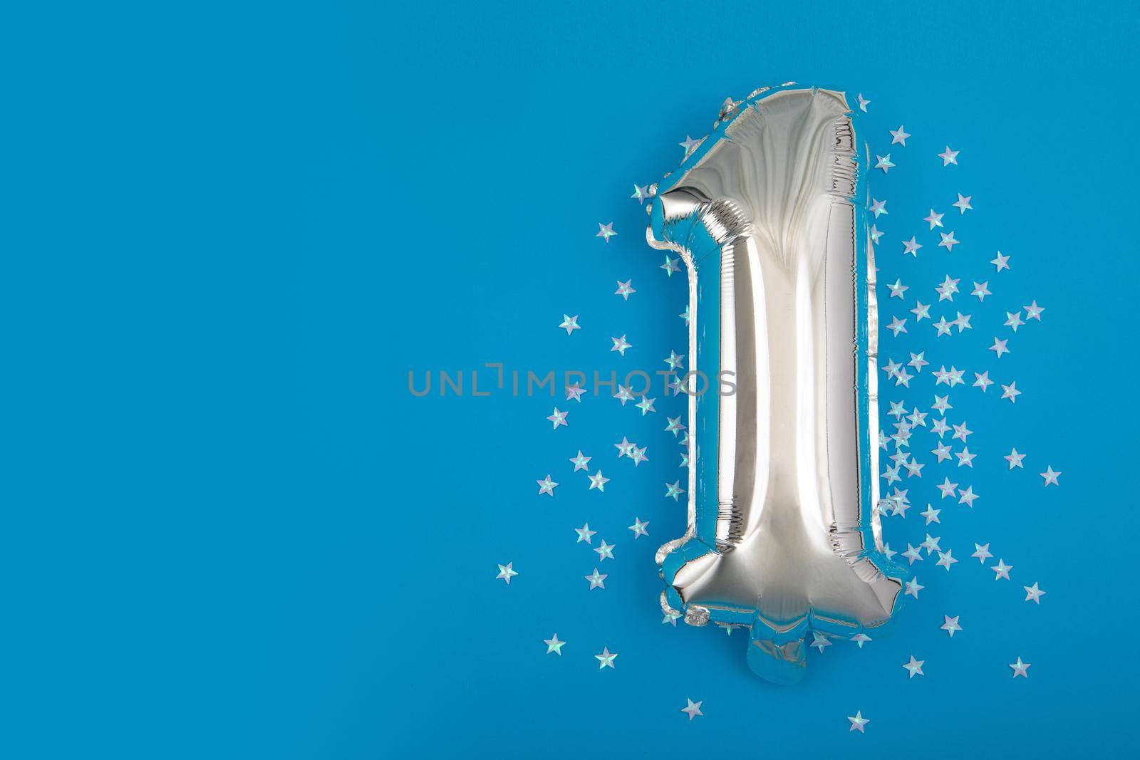 Silver balloon 1 on a blue background with confetti stars. Number One 1. Holiday Party Decoration or postcard concept with top view on blue background