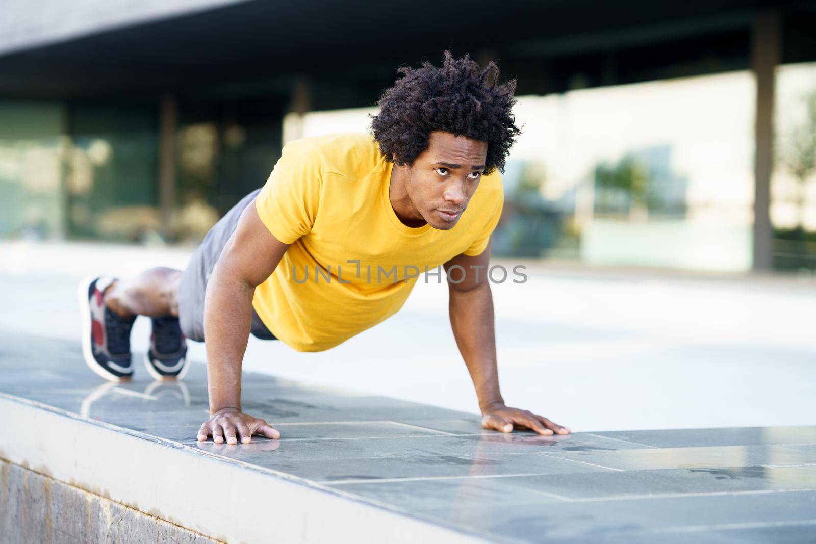 Black man doing triceps dip exercise on city street bench. by javiindy