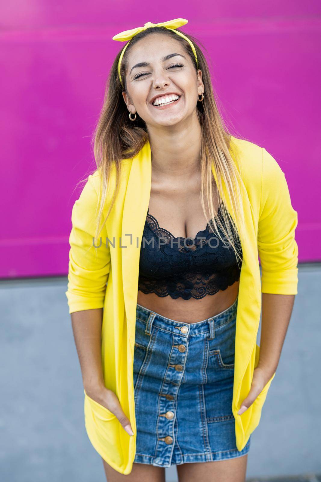 Happy woman wearing a yellow jacket and headband, near an urban purple wall