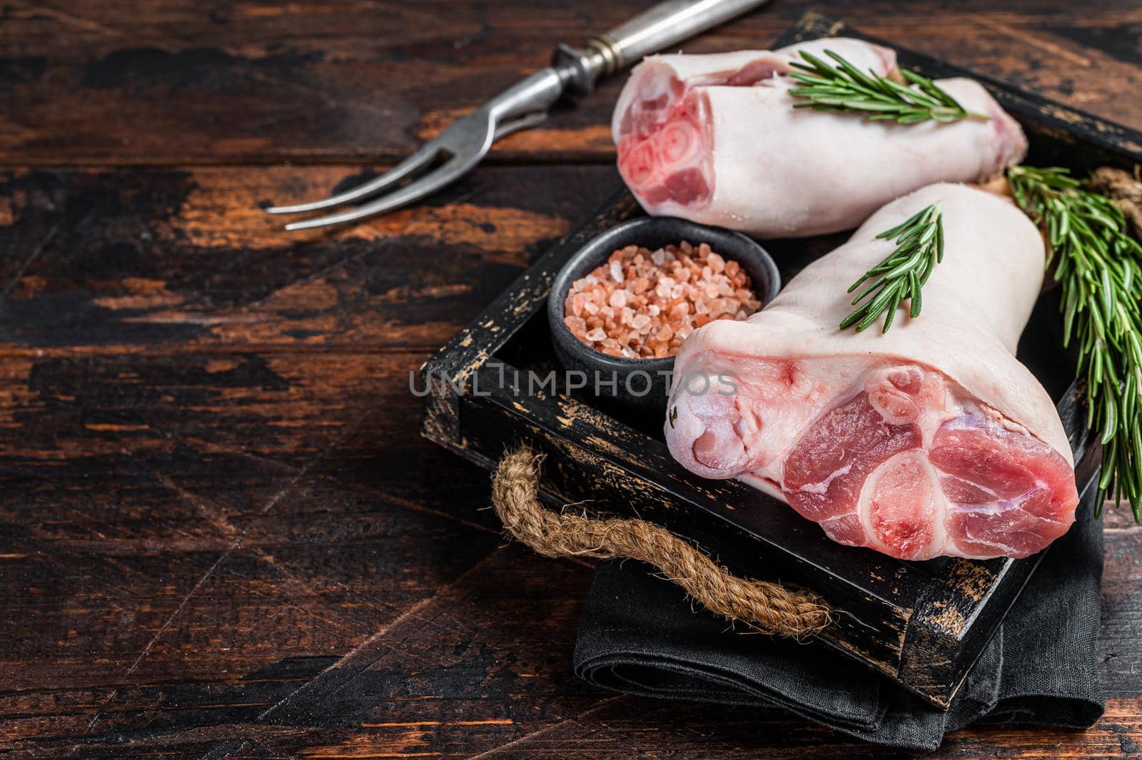 Uncooked Raw pork hoof, knuckle, feet in a wooden tray with herbs. Wooden background. Top view. Copy space.