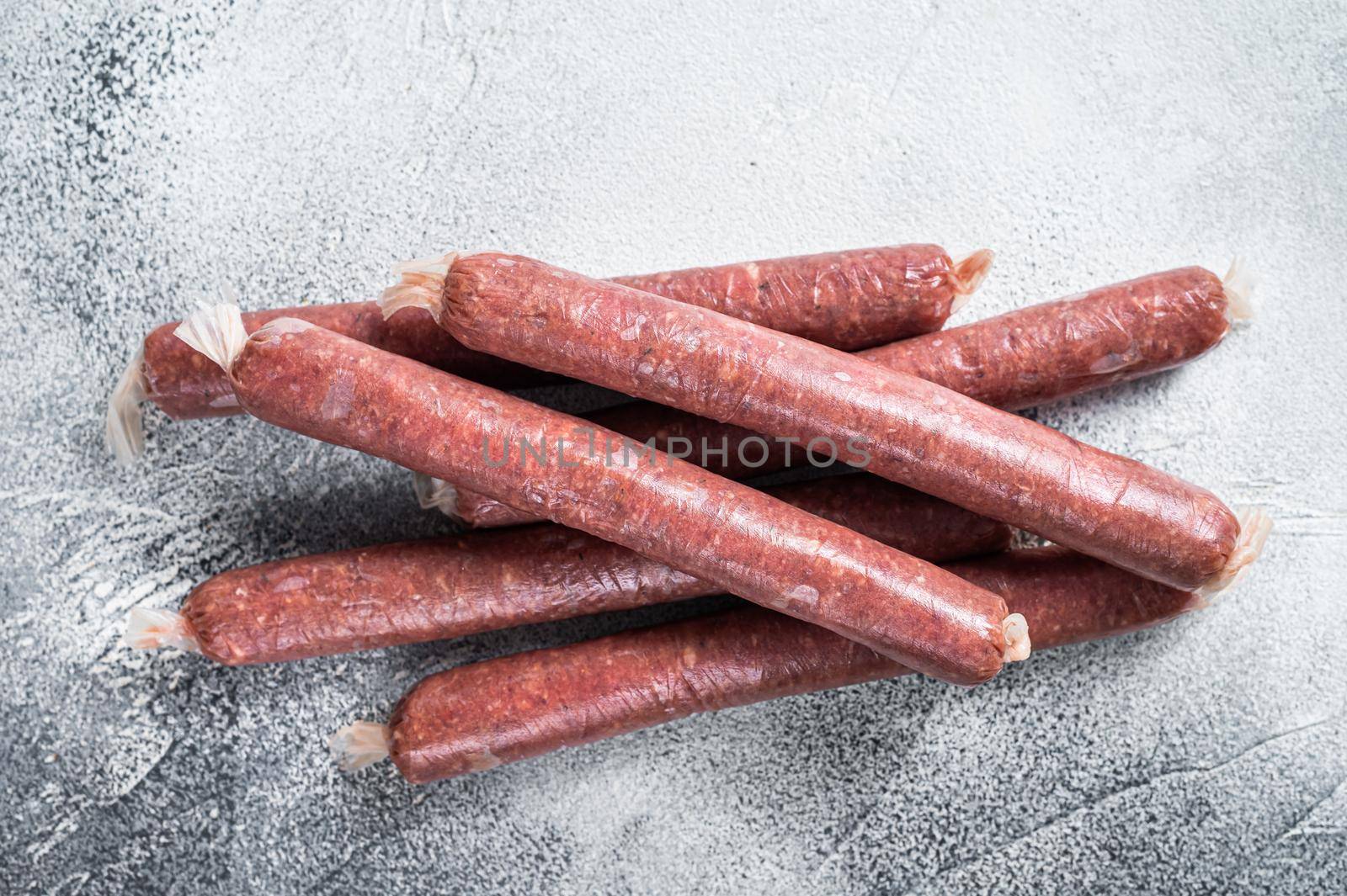 Raw butchers sausages in skins with herbs on kitchen table. White background. Top view.