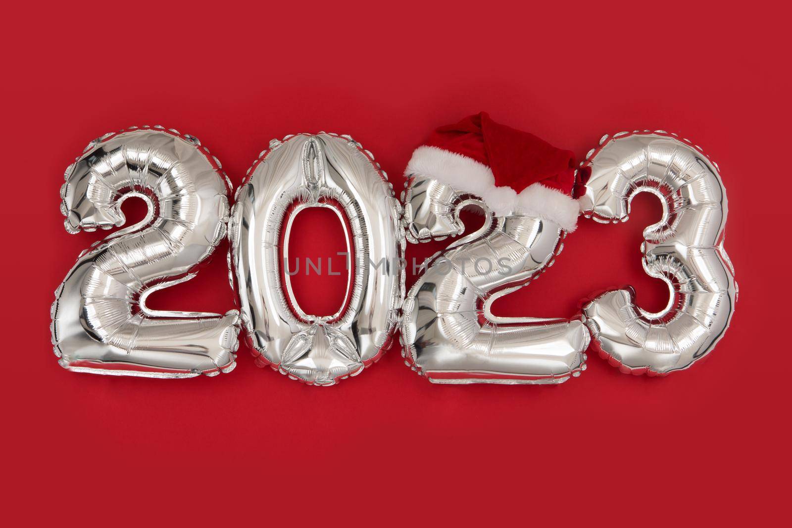 2023 inflatable balloons on red background with santa hat. Happy New year 2023 celebration. Silver foil balloons numeral 2023. Postcards and posters Copy space