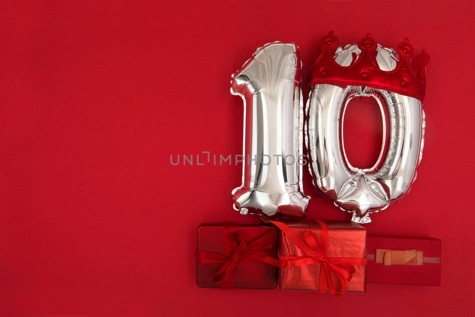 Foil silver air balloons showing number 10 ten placed on red background with wrapped presents for concept of birthday anniversary