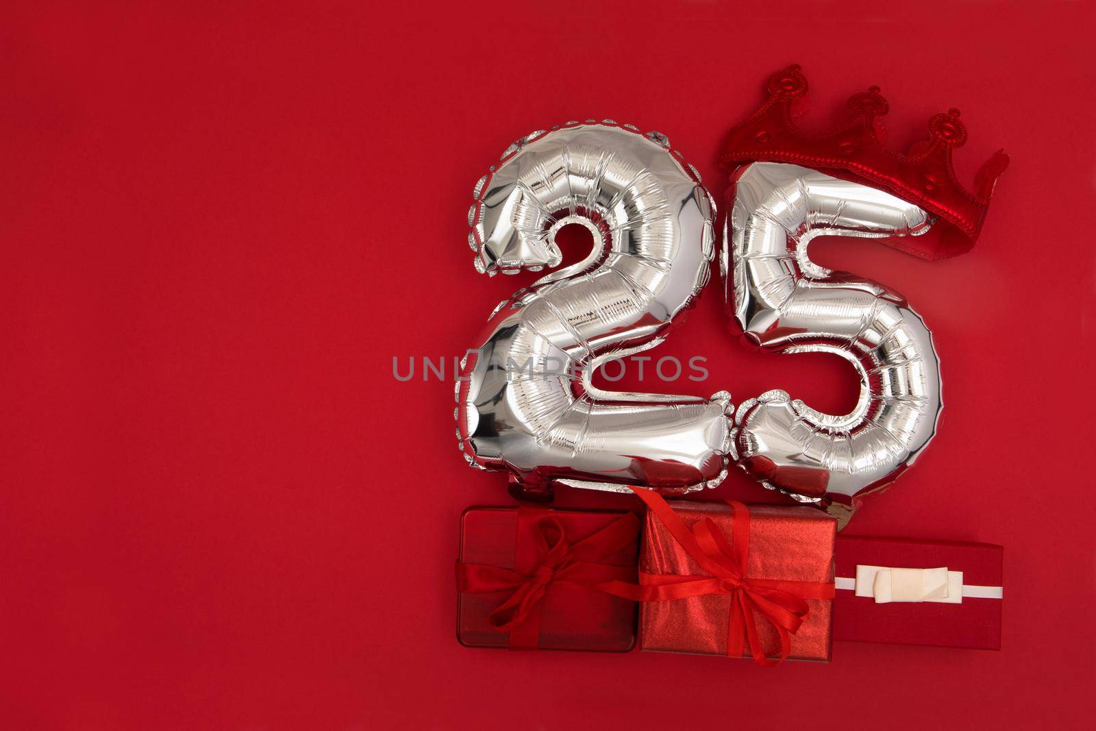 Foil silver air balloons showing number 25 twenty five placed on red background with wrapped presents for concept of birthday anniversary