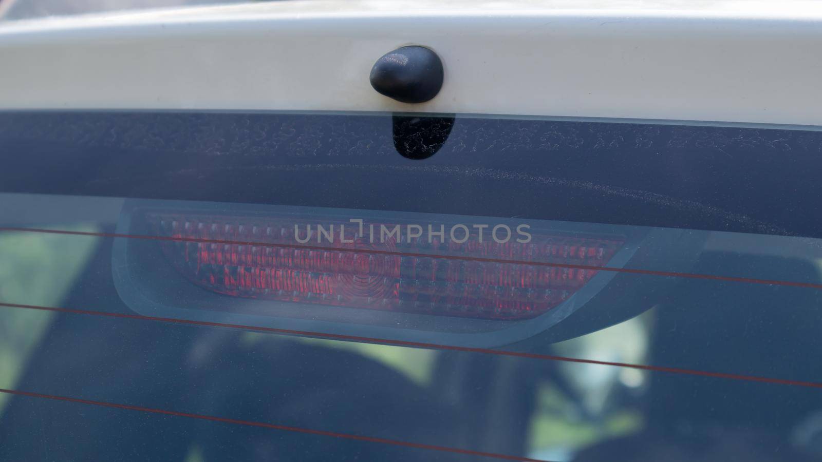 Rear window of a dusty white car with a stoplight behind glass, close-up. Red signals indicating vehicle braking. They turn on automatically when you press the brake and turn off when you release it. by Roshchyn