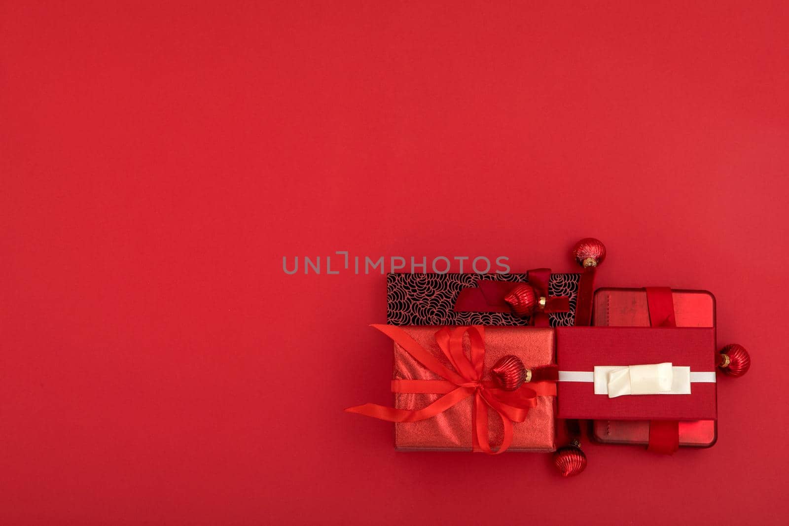 Top view composition of various Christmas presents wrapped in paper with ribbons and decorative balls placed on bright red surface with empty space