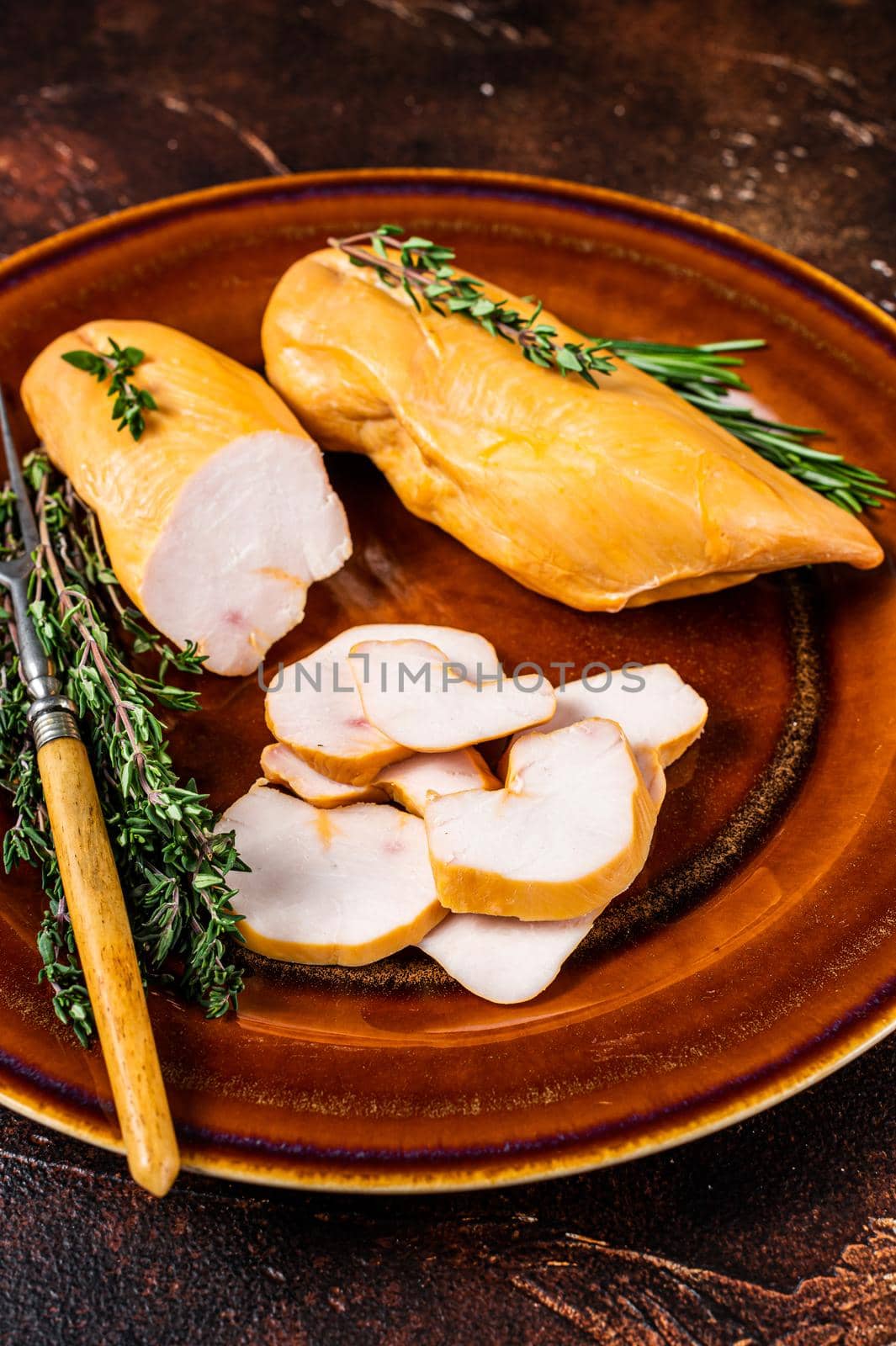 Hot Smoked chicken breast Poultry meat in a rustic plate with herbs. Dark background. Top view.