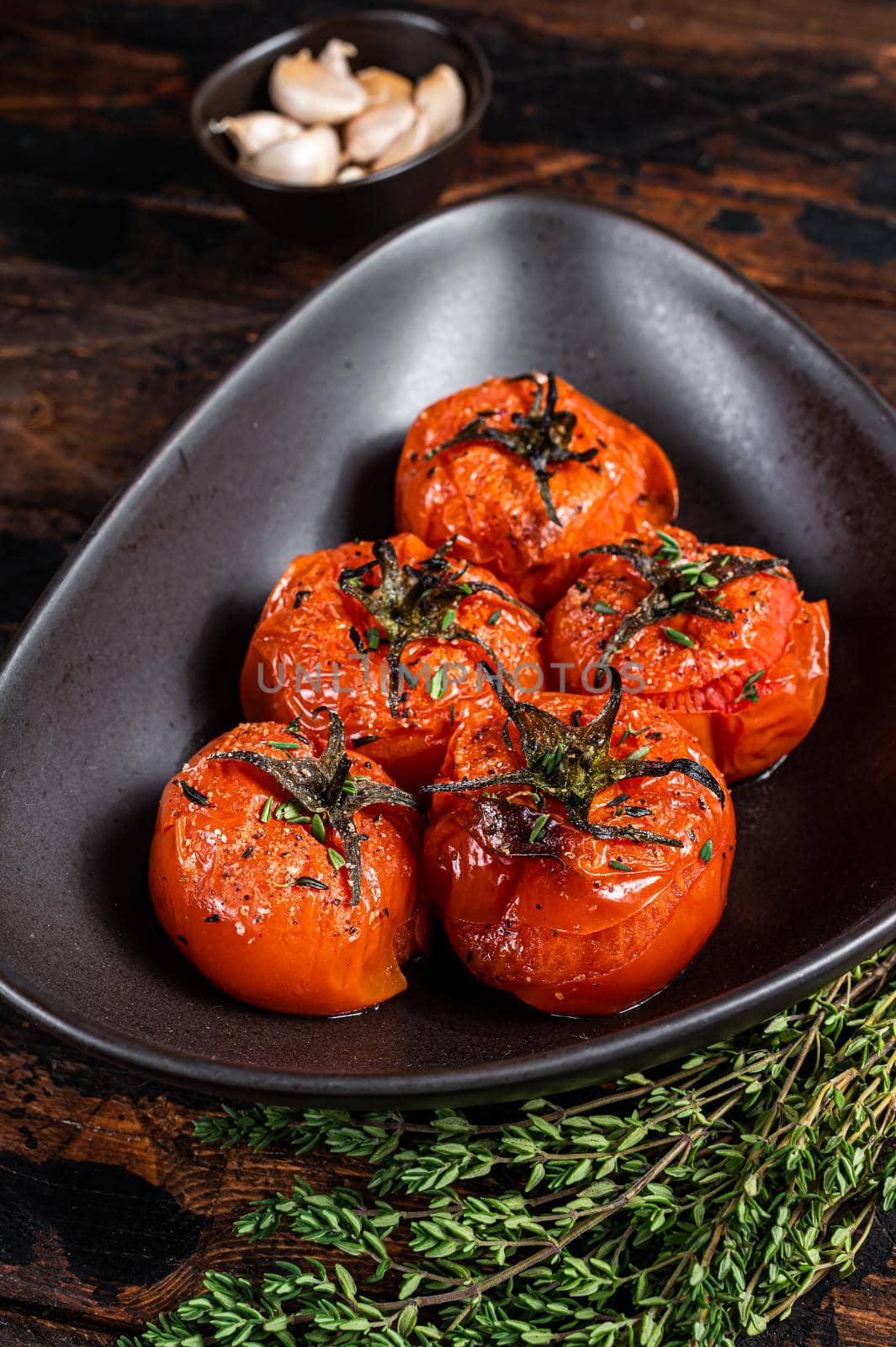 Oven Roasted cherry tomatoes with thyme and garlic in a plate. Dark wooden background. Top view by Composter