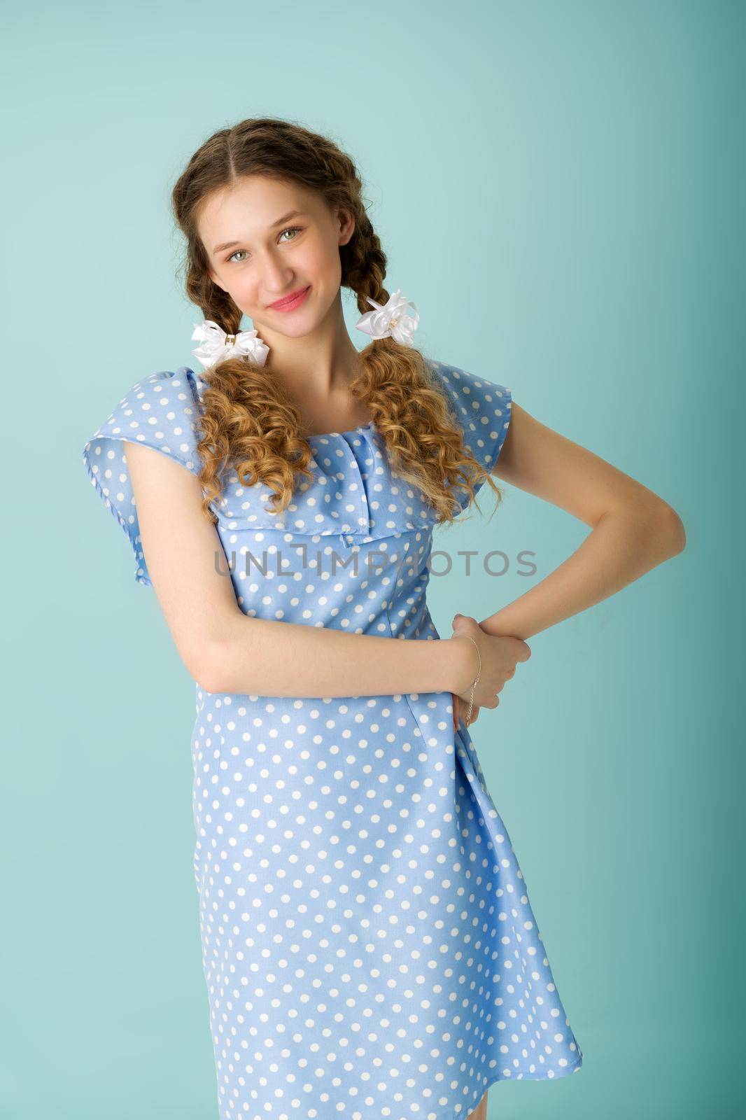 Portrait of a cheerful teenage girl in a blue dress. Happy girl in polka dot dress looking up with positive facial expression over isolated blue background.close-up